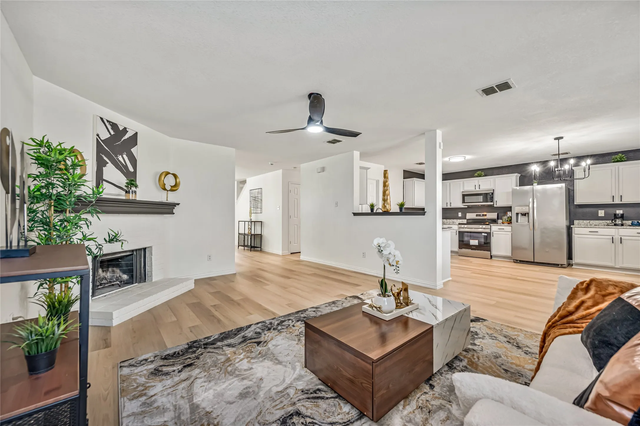 Open-concept living space featuring wood-finish flooring, a corner fireplace with a mantel, and a ceiling fan