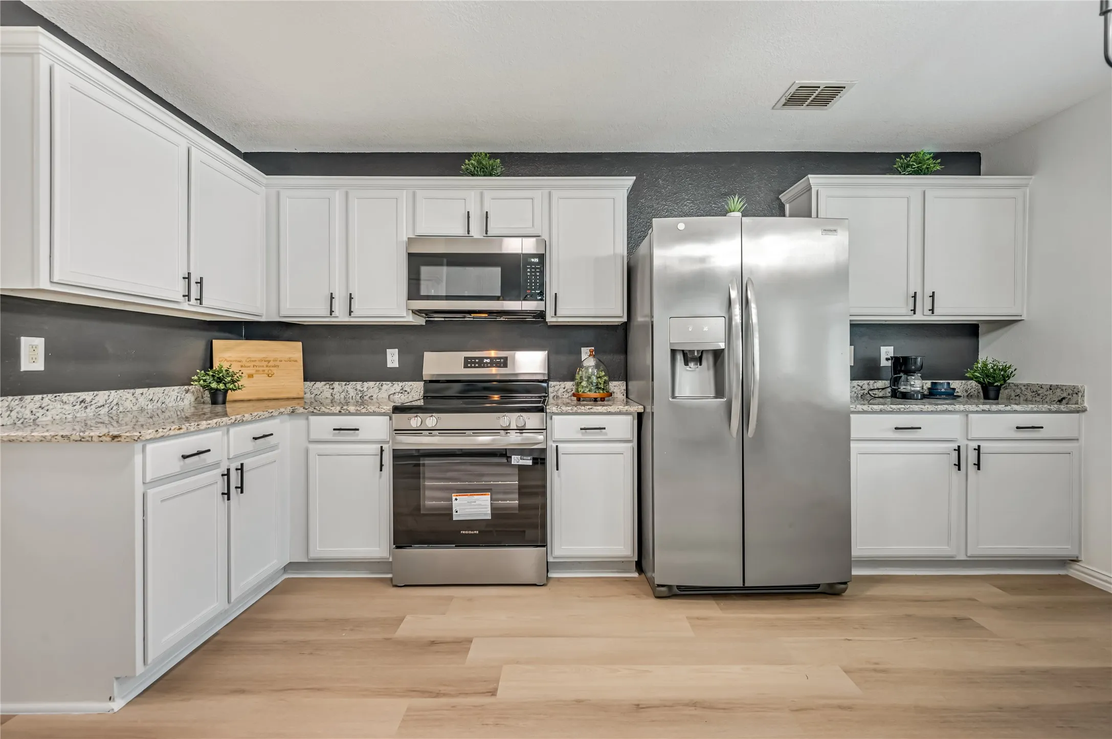 White cabinetry with black hardware, stainless steel appliances, speckled countertops, and wood-finish flooring