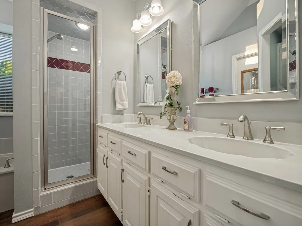 Dual rectangular mirrors, a double vanity with white cabinetry, a light-colored countertop, and brushed nickel hardware