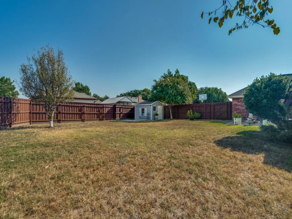 Expansive backyard featuring a privacy fence, mature trees, and an accessory storage shed