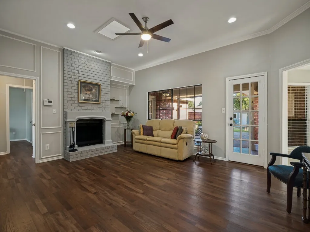 Living area featuring wood-finish flooring, a brick fireplace with a mantel, crown molding, a ceiling fan, and a French door with multiple lites
