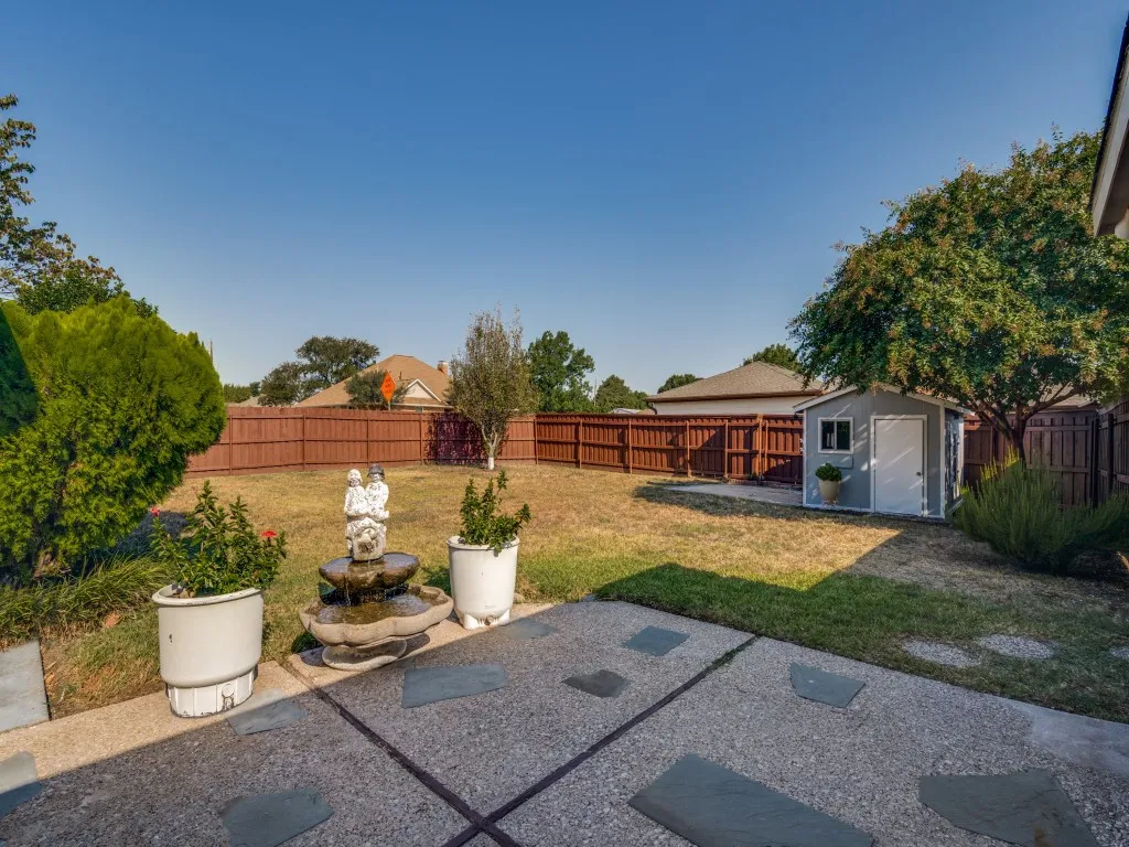Expansive backyard featuring a privacy fence, mature trees, a storage shed, and a stone patio