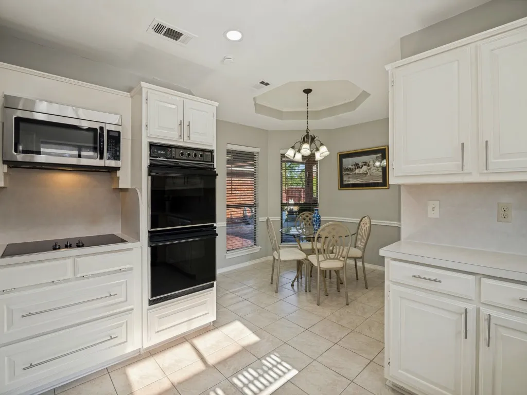 White cabinetry, stainless steel microwave, built-in double oven, integrated cooktop, and neutral tile flooring