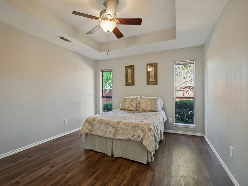Tray ceiling with a ceiling fan light fixture, rich wood-finish flooring, and two windows providing natural light