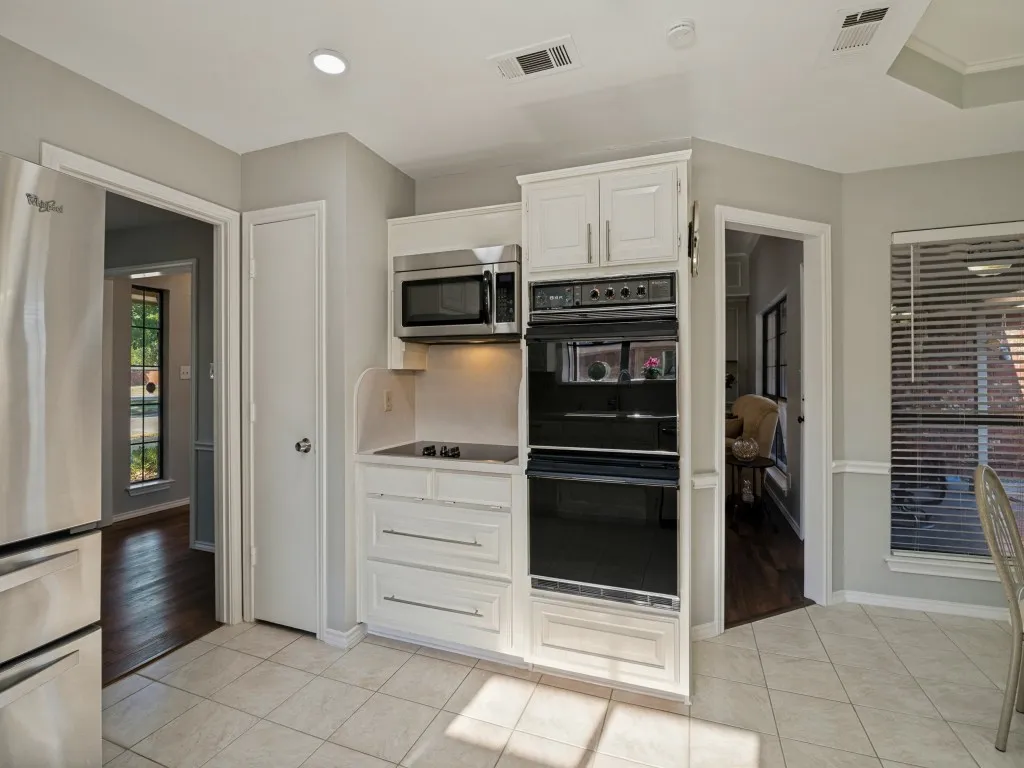 Kitchen featuring white cabinetry, stainless steel appliances, built-in double ovens, and tile flooring