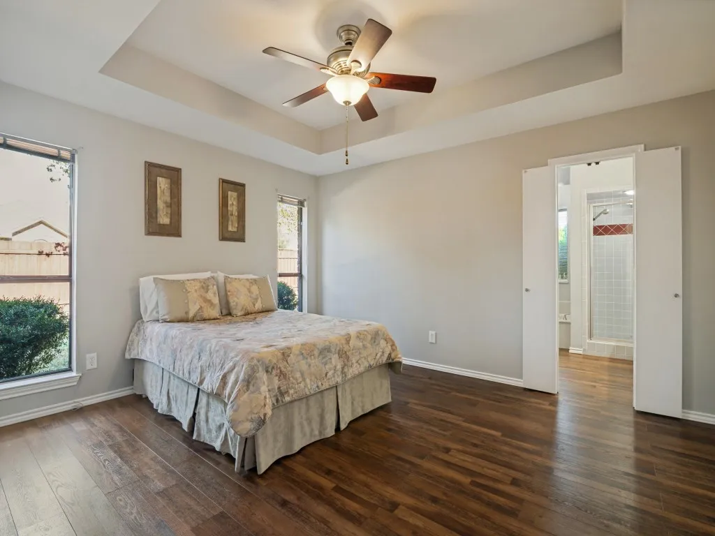 Tray ceiling with a ceiling fan, wood-finish flooring, and a shower with white tile and red accent tile