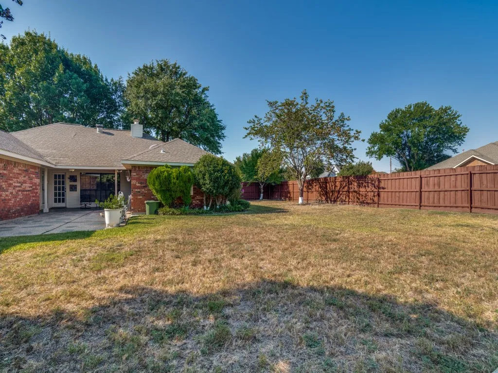 Expansive backyard featuring a wood privacy fence, a covered patio, and mature trees