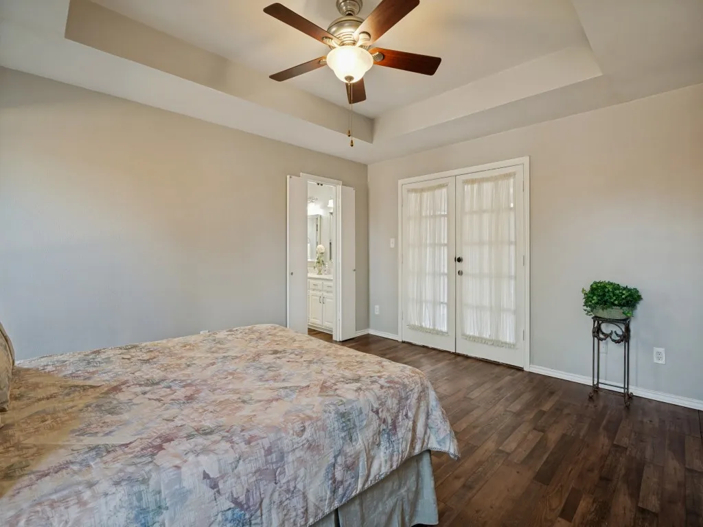 Tray ceiling with a ceiling fan light fixture, wood-finish flooring, and French doors