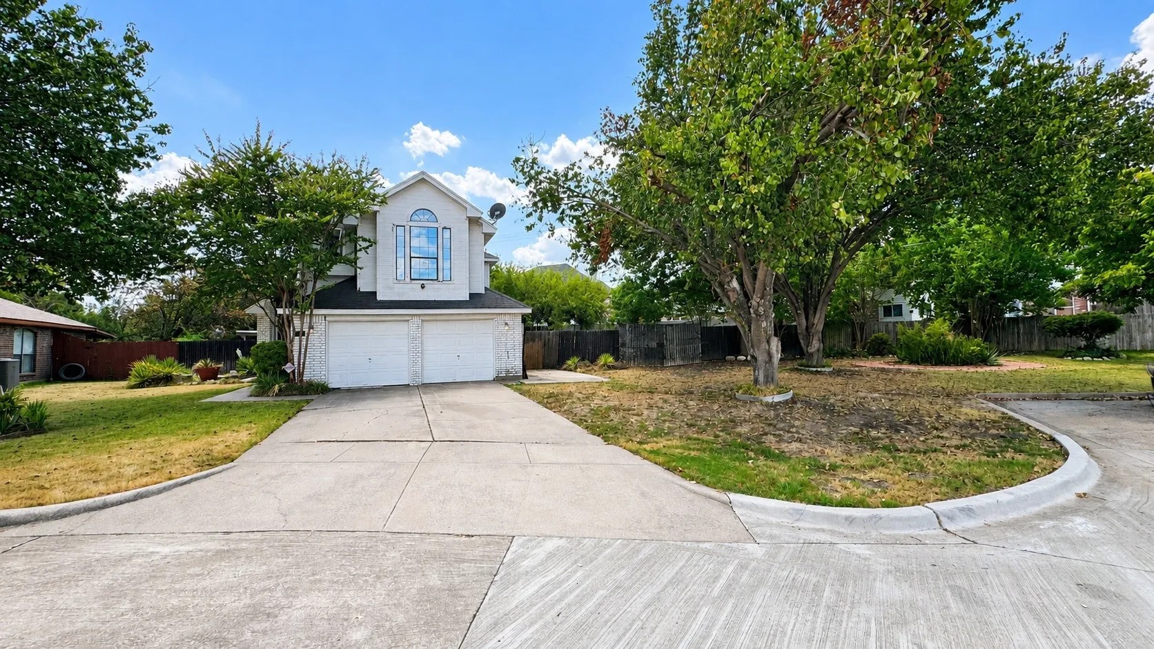 Two-story stucco facade featuring a dual garage, arched window, and mature trees