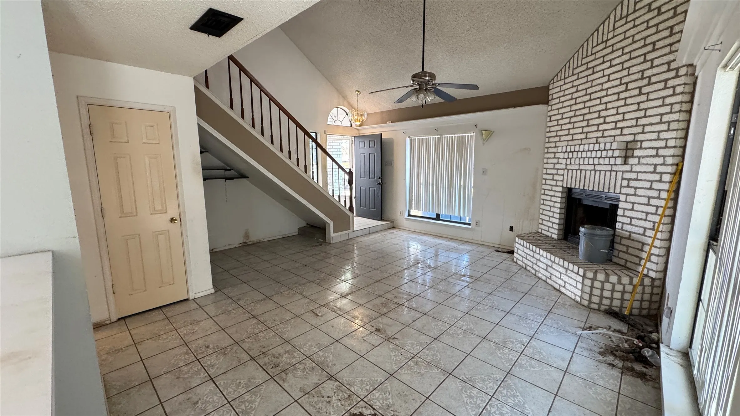 Vaulted ceilings, a substantial brick fireplace, a ceiling fan, and tiled flooring