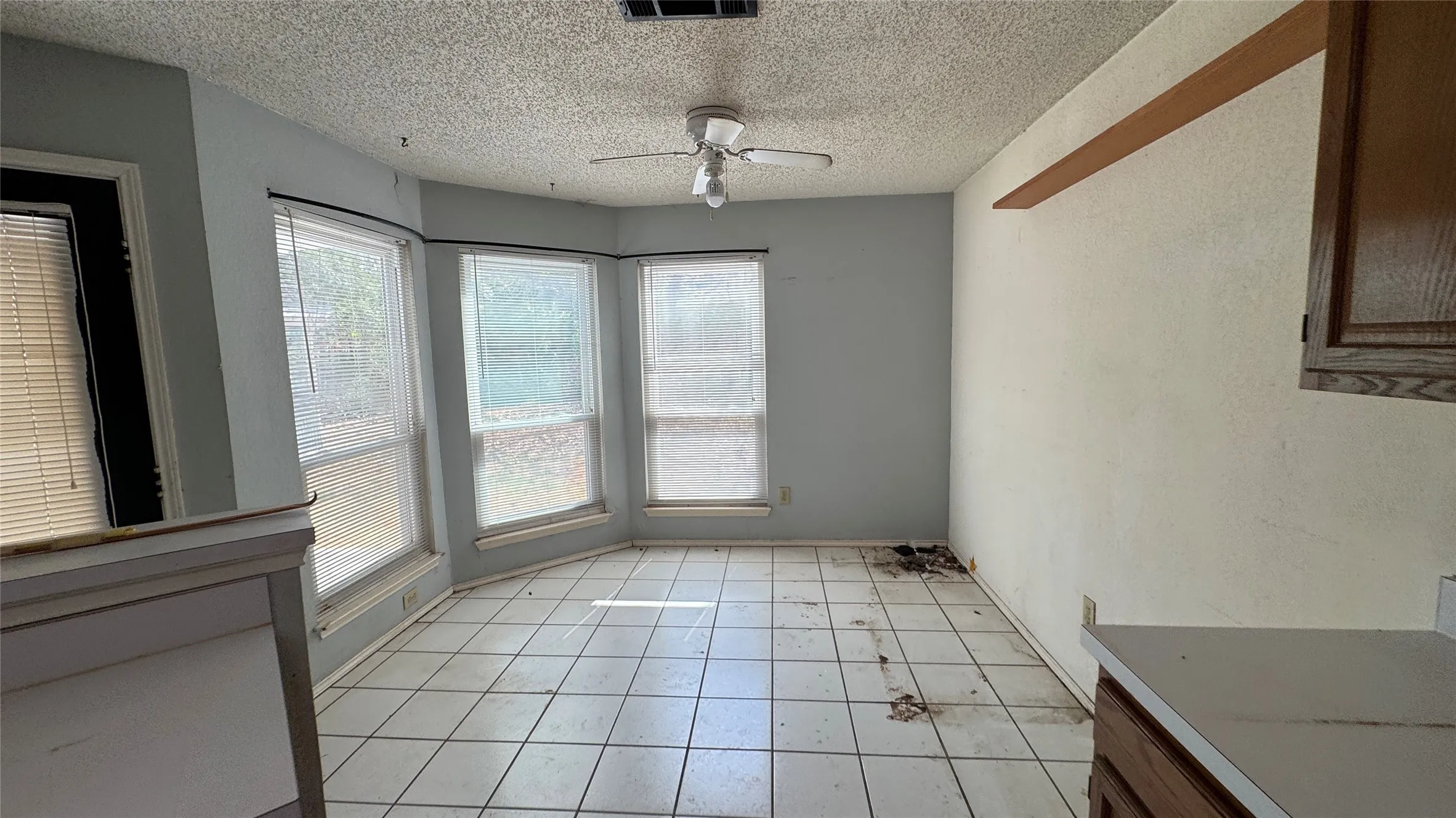 Bay window wall with multiple windows, ceiling fan, and tiled flooring