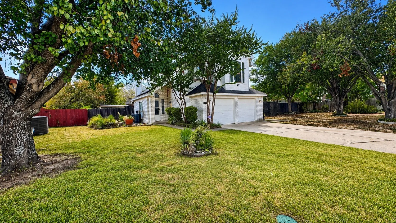 White brick exterior with a two-car garage, concrete driveway, and mature landscaping