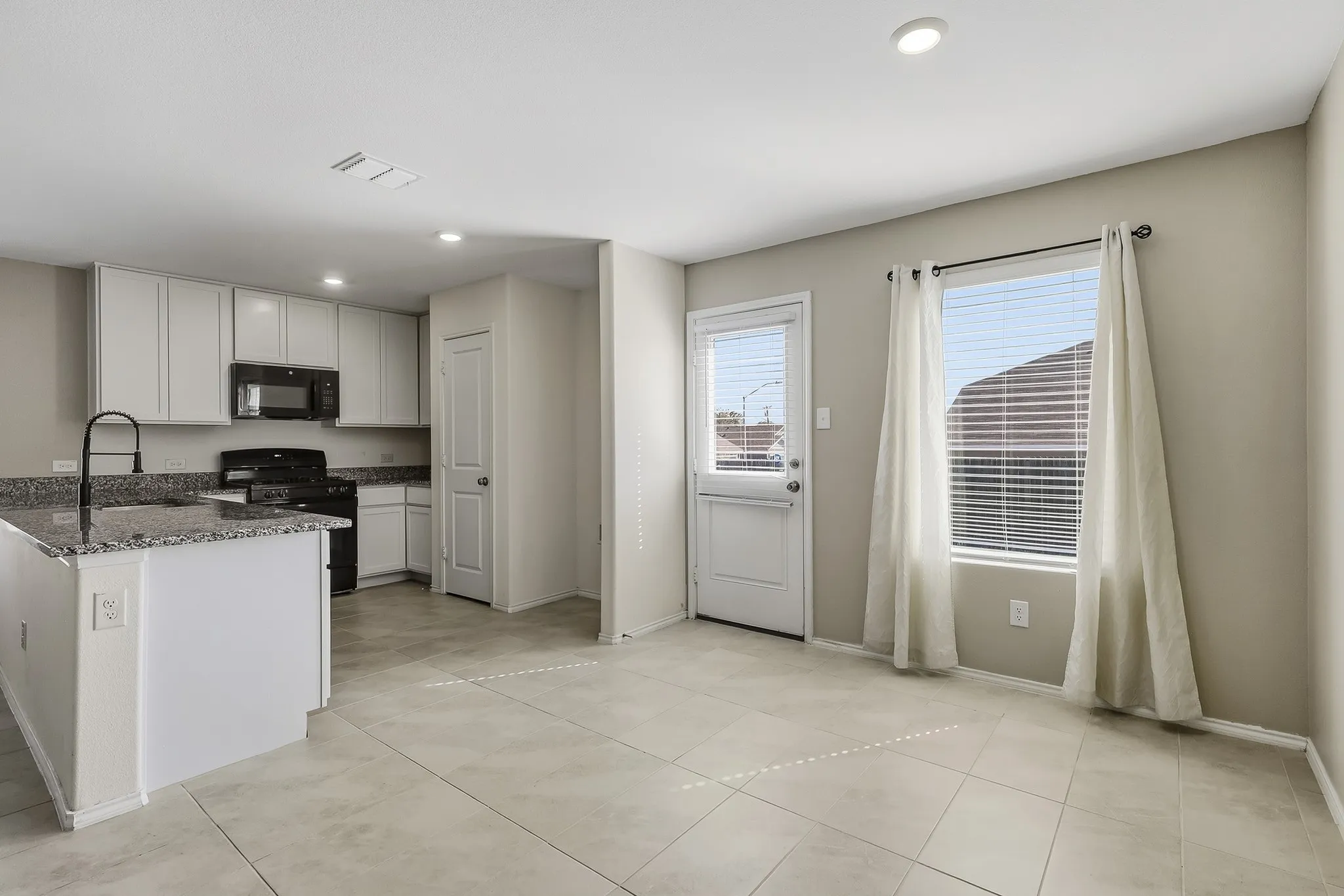 Kitchen featuring white cabinetry, dark stone countertops, black appliances, a kitchen island, and recessed lighting
