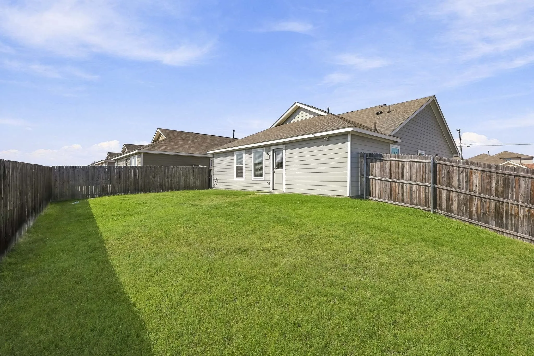 Expansive grassy yard with wood fencing and a light-colored siding exterior