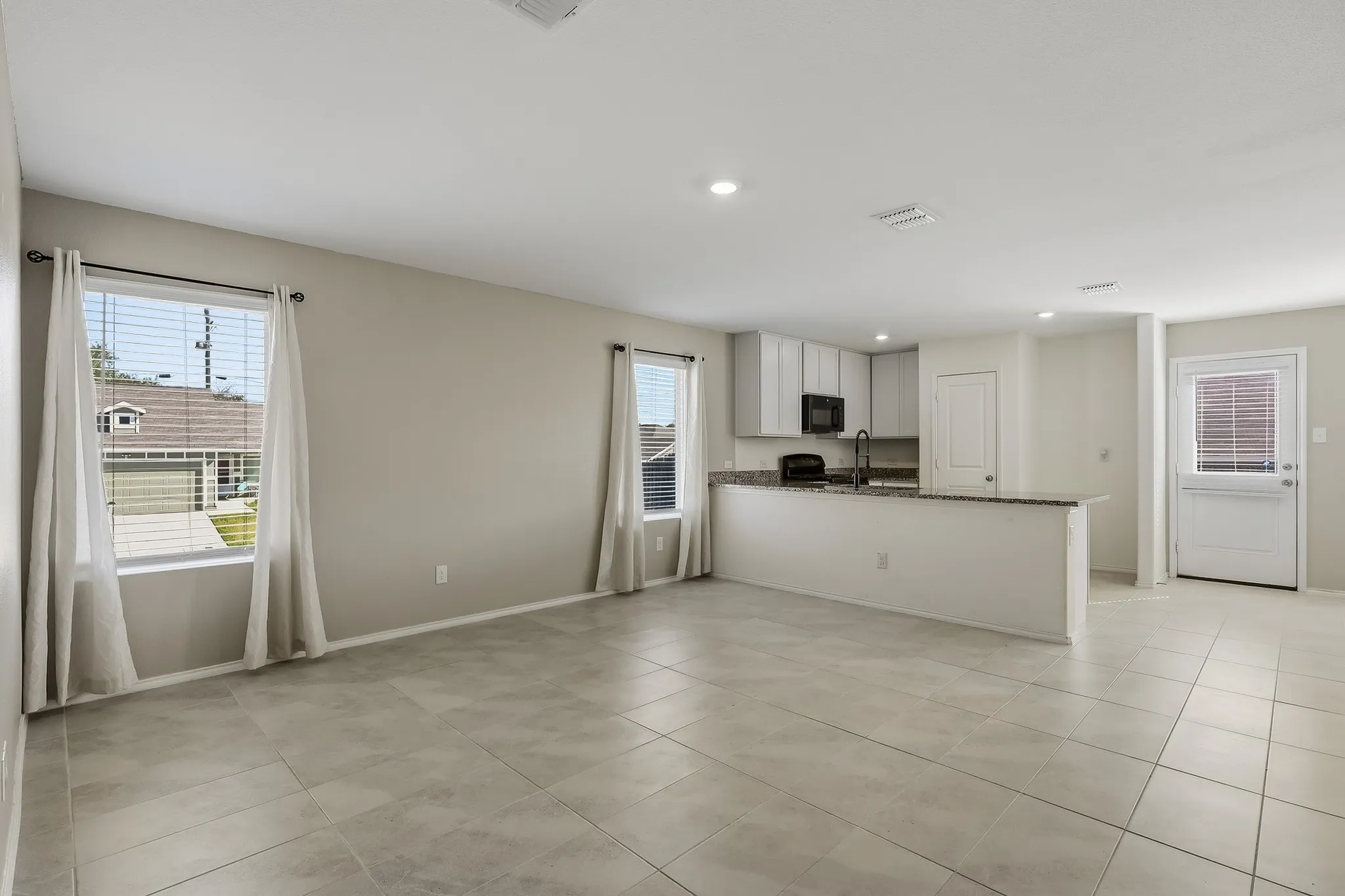 Open-concept living area with tiled flooring, recessed lighting, and a kitchen featuring a peninsula with countertop seating, light-toned cabinetry, and dark-finish appliances