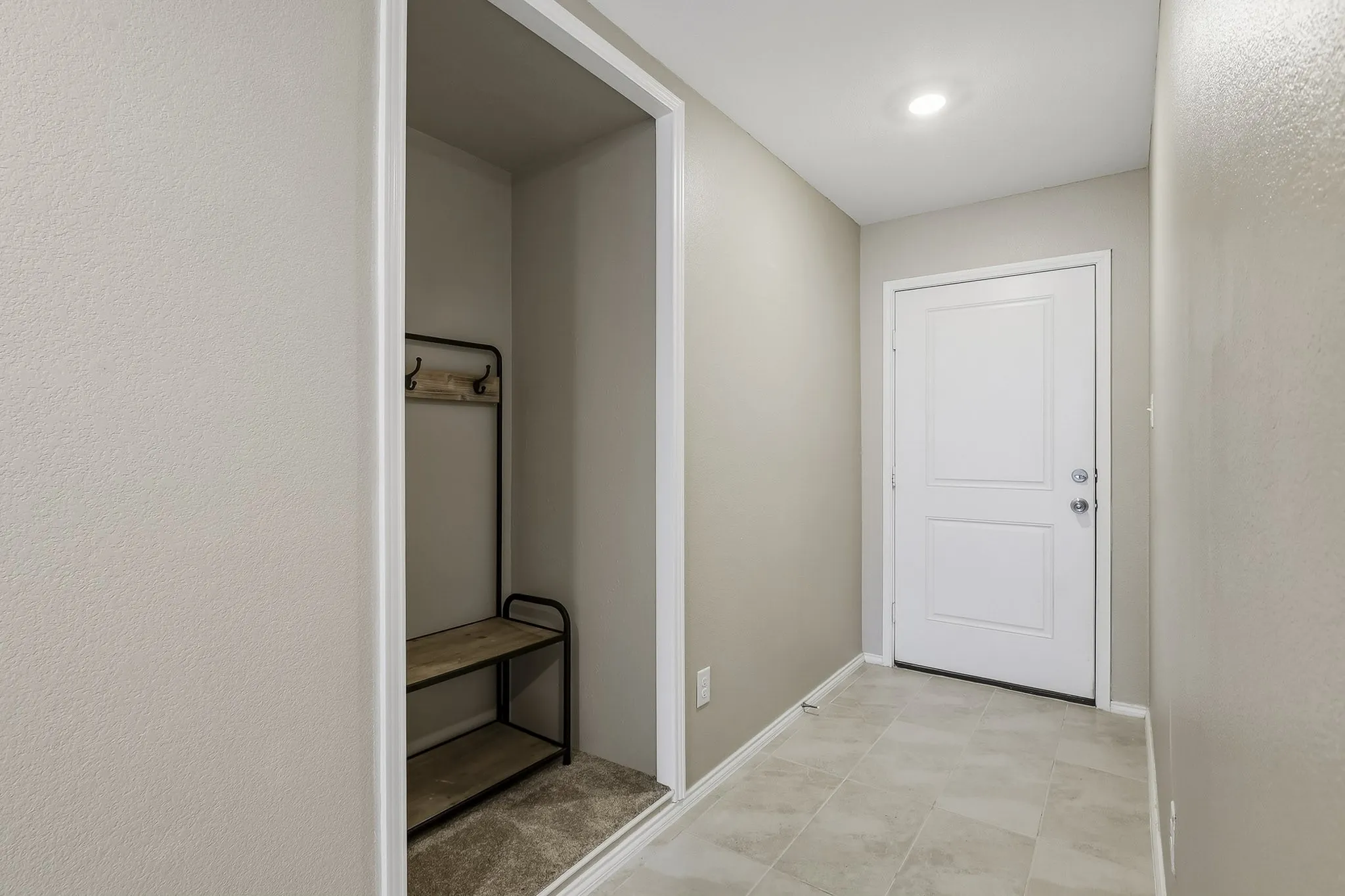 Recessed lighting illuminates the tiled entry, featuring a paneled door and neutral wall tones