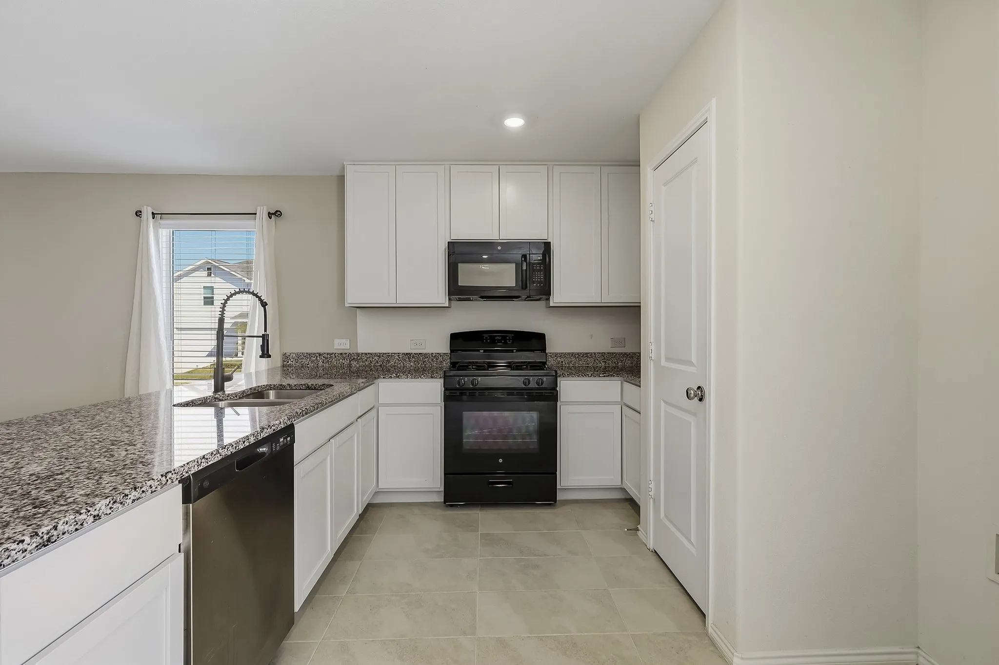 Kitchen featuring white cabinetry, speckled countertops, stainless steel sink with a high-arch faucet, black range, and black microwave