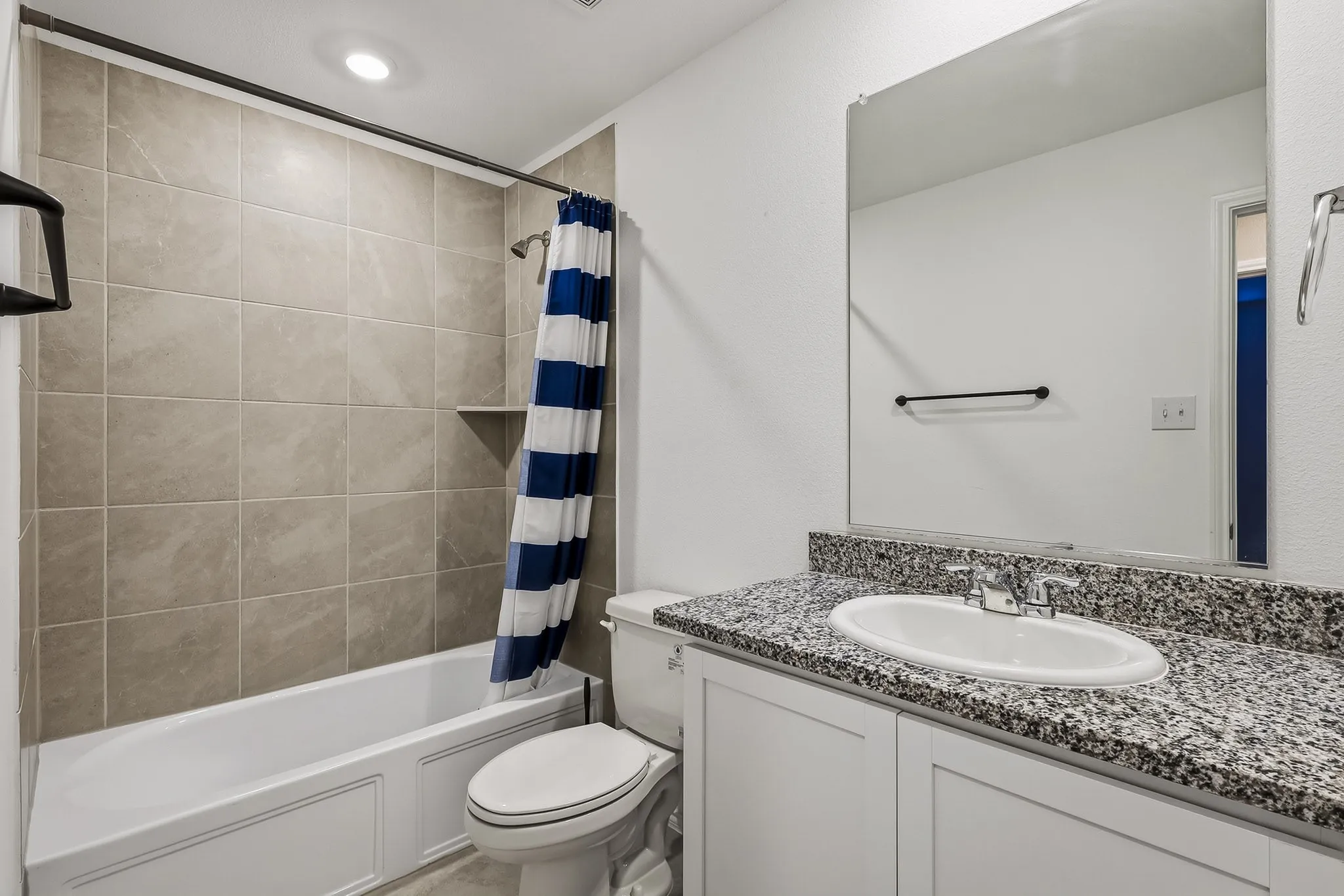 Bathroom featuring a shower-tub combination with tile surround, a built-in shower niche, a white vanity with a granite-style countertop, and an integrated sink