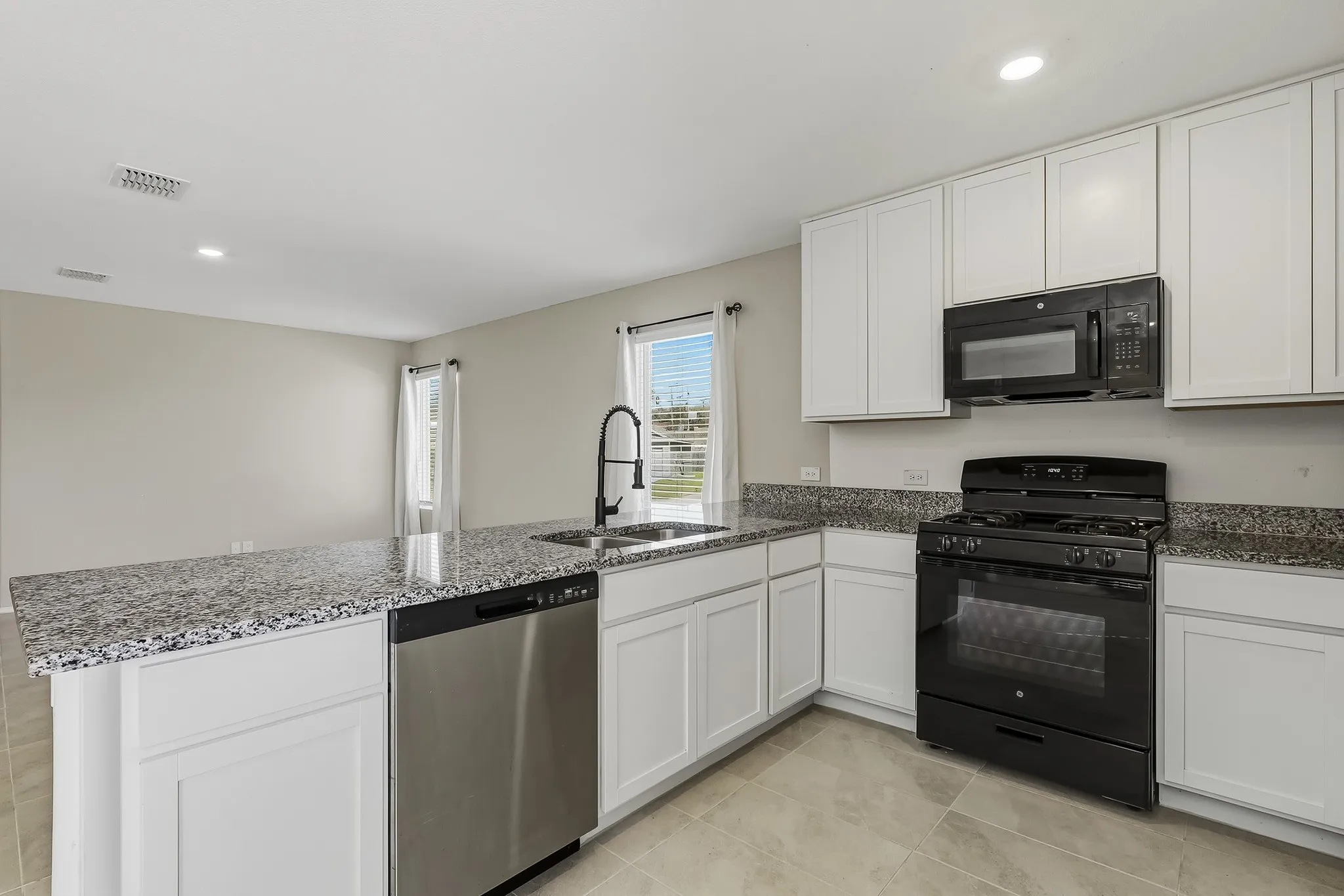 Kitchen featuring light-toned cabinetry, dark speckled countertops, stainless steel dishwasher, black range, and black built-in microwave
