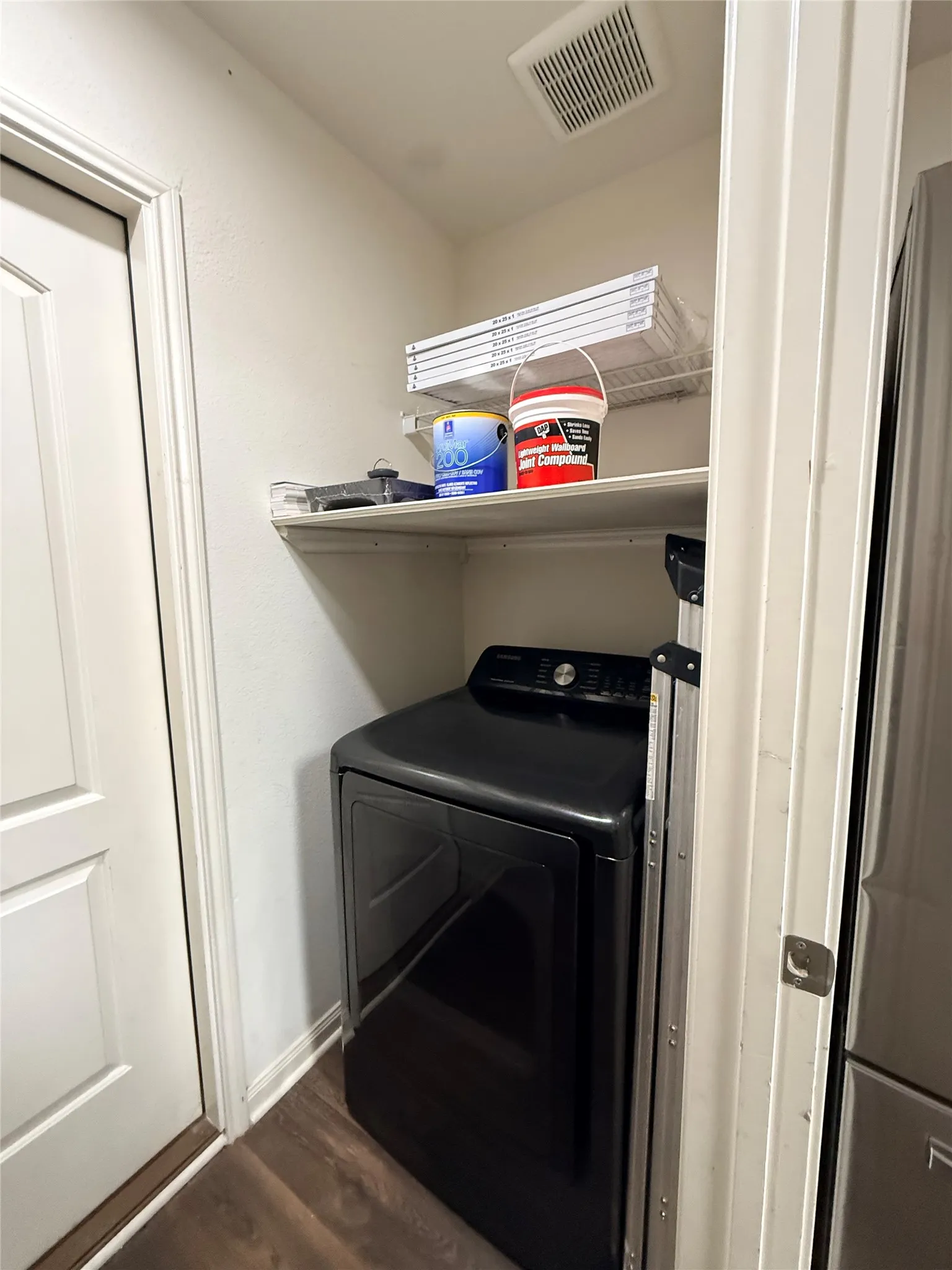 Laundry area featuring a black appliance, wood-finish flooring, and integrated wire shelving