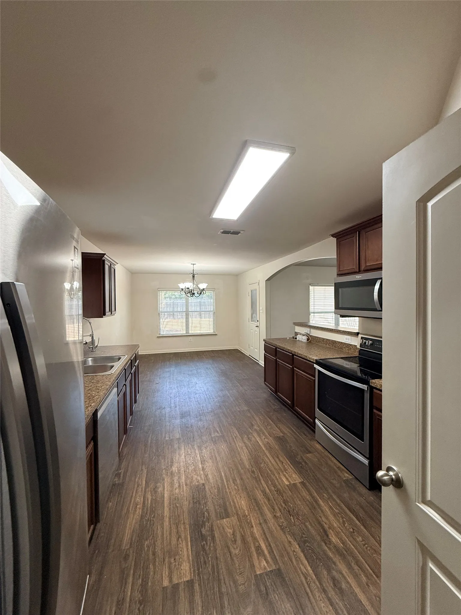 Kitchen featuring wood-finish flooring, dark wood cabinetry, stainless steel appliances, and a double basin sink