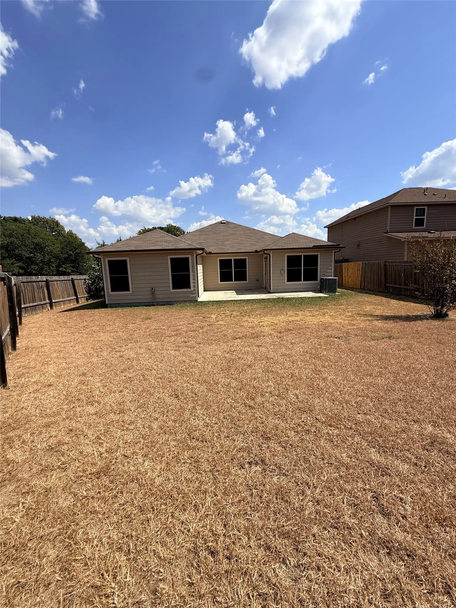 Rear exterior with beige siding, multiple windows, and a patio area