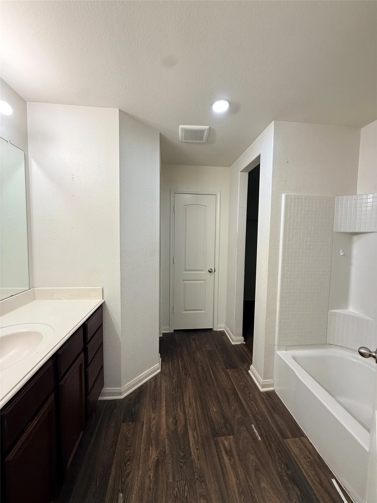 Wood-finish flooring, recessed lighting, built-in vanity with single basin sink, white tile shower surround, and a built-in tub