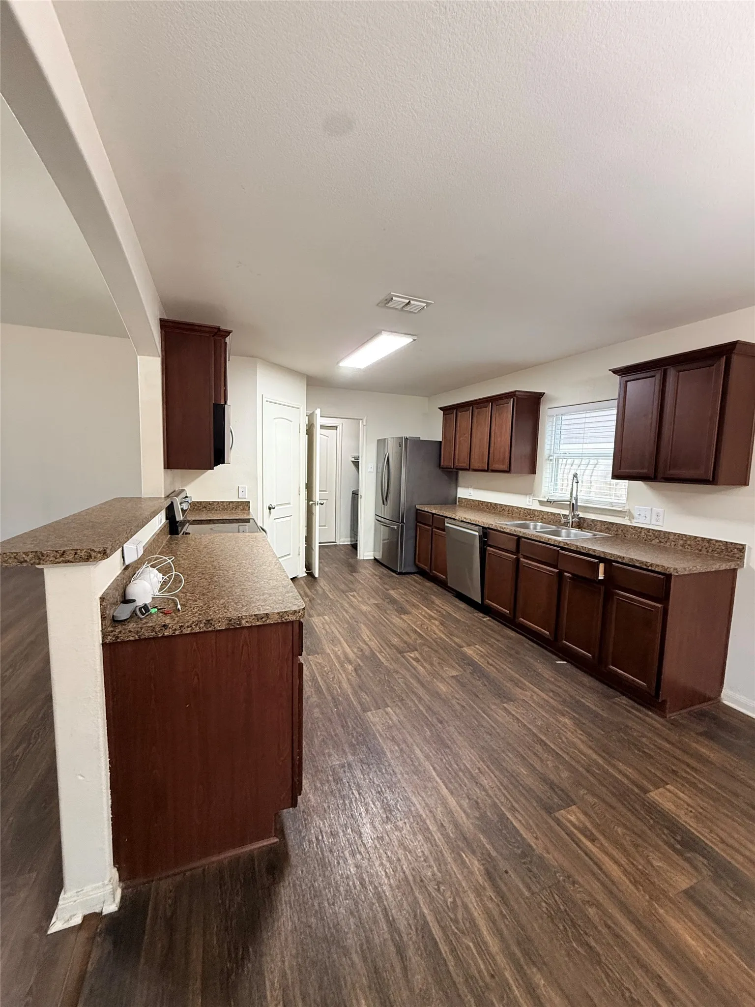 Open-concept kitchen with wood-finish flooring, dark wood cabinetry, granite-style countertops, and stainless steel appliances