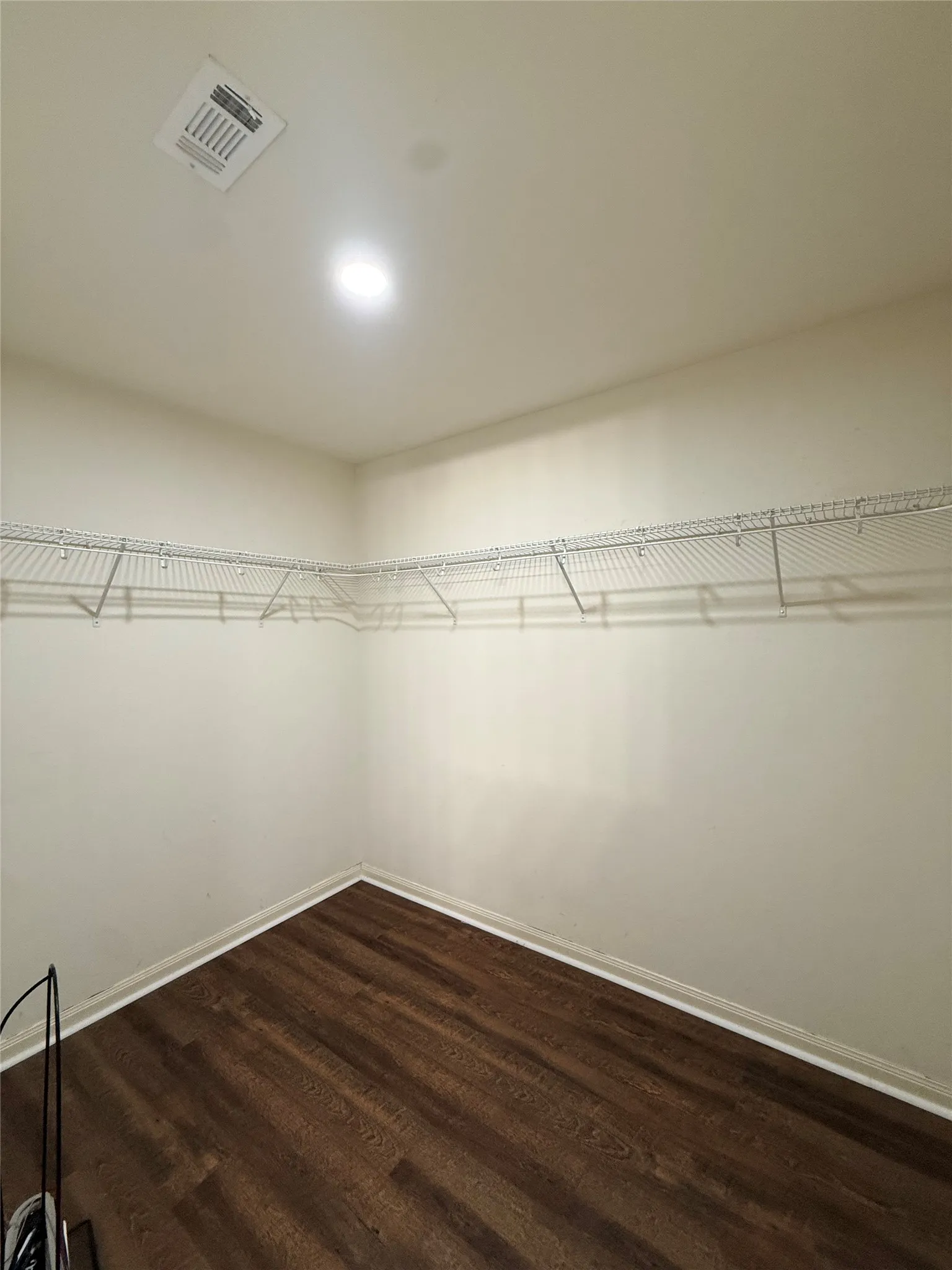 Primary closet Wood-finish flooring, white walls, built-in wire shelving, recessed lighting, and a ceiling vent