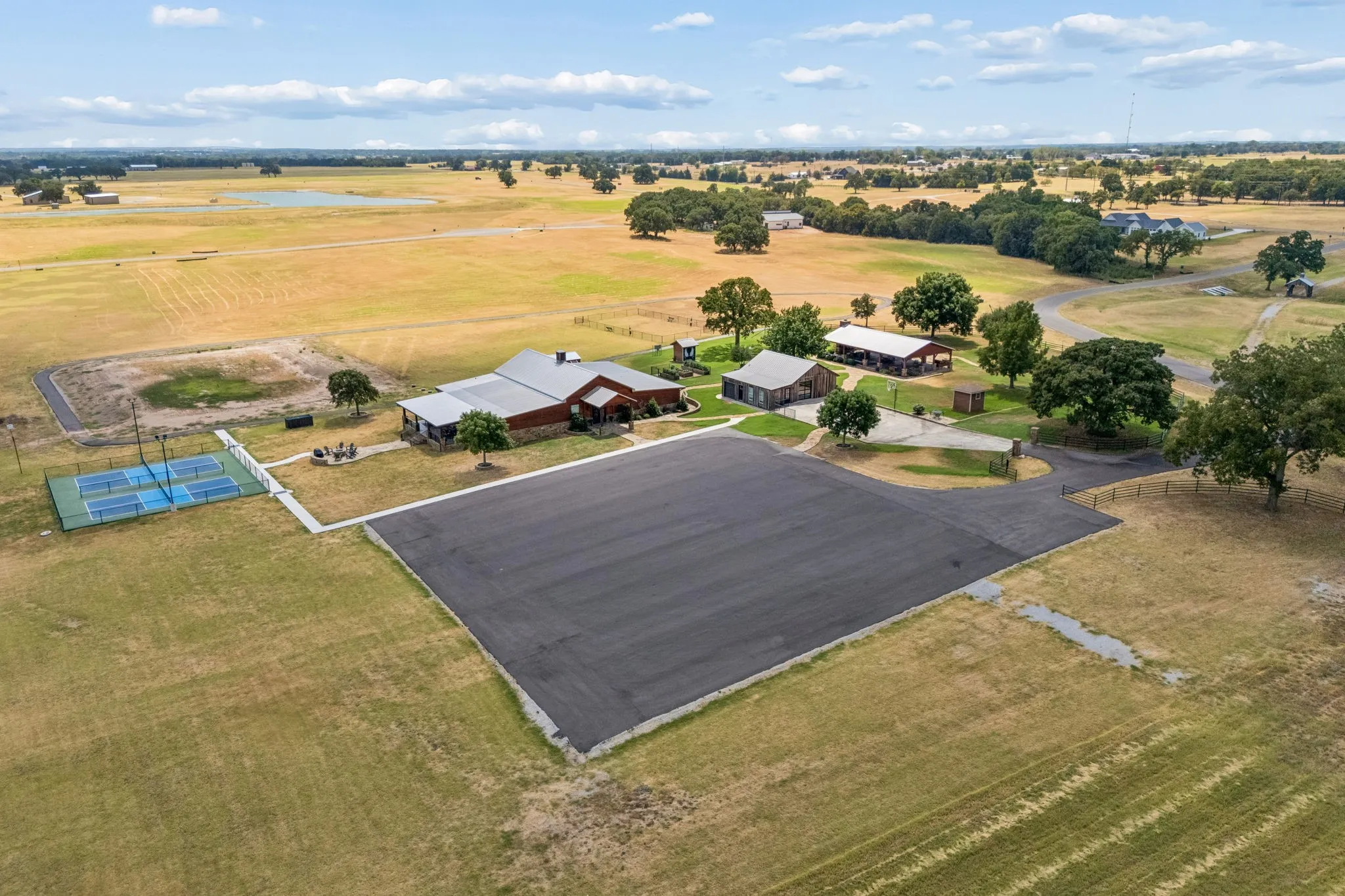 Expansive property featuring multiple structures, a paved drive, a concrete patio, and a dedicated pickleball court