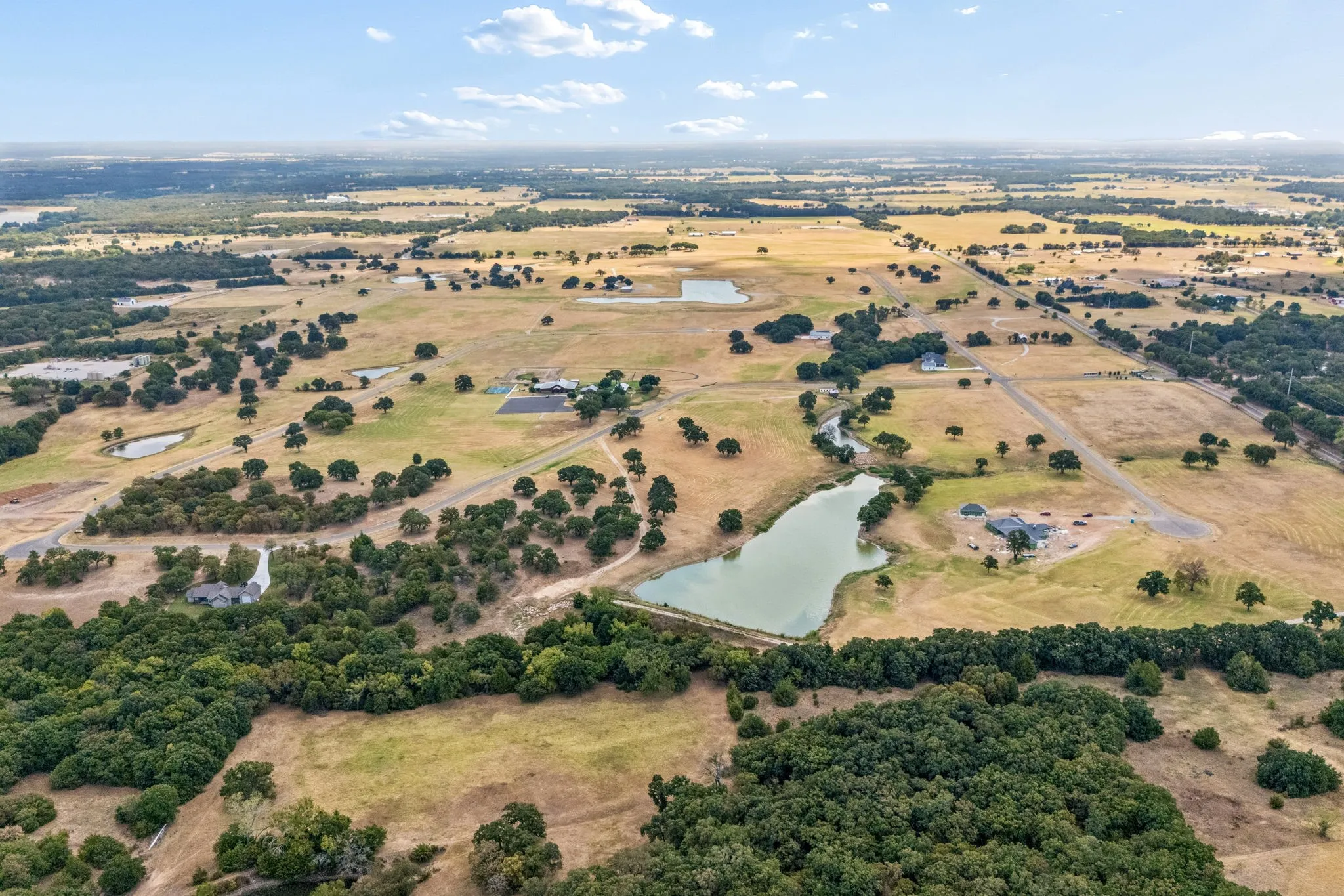 Expansive rural landscape featuring multiple bodies of water, scattered trees, and visible residential structures