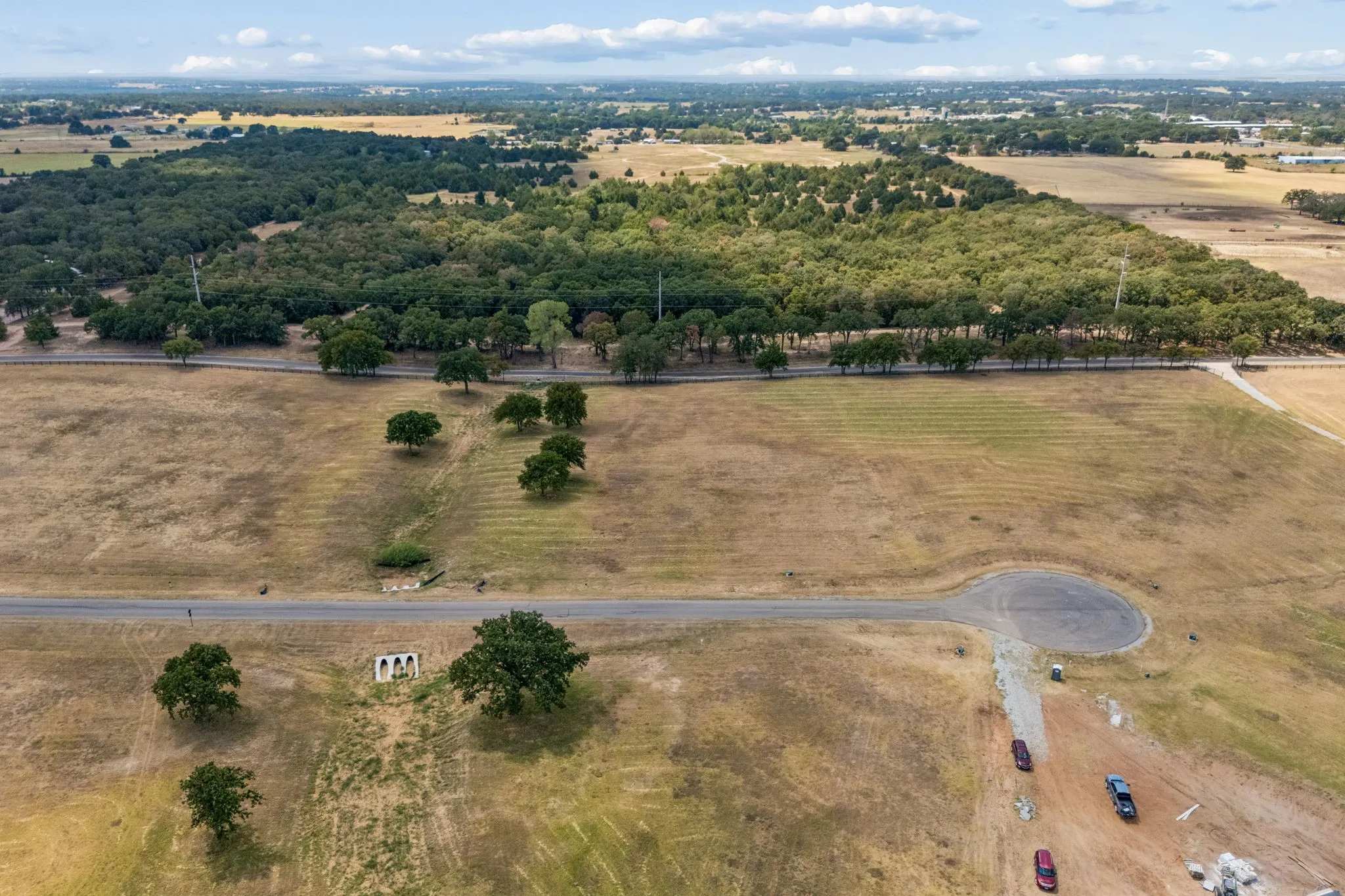 Expansive land with a paved road, mature trees, and a distant forested area