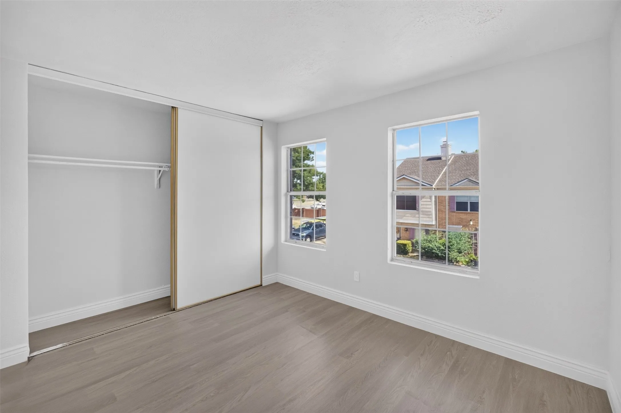 Recessed closet with sliding doors, two windows, and wood-finish flooring