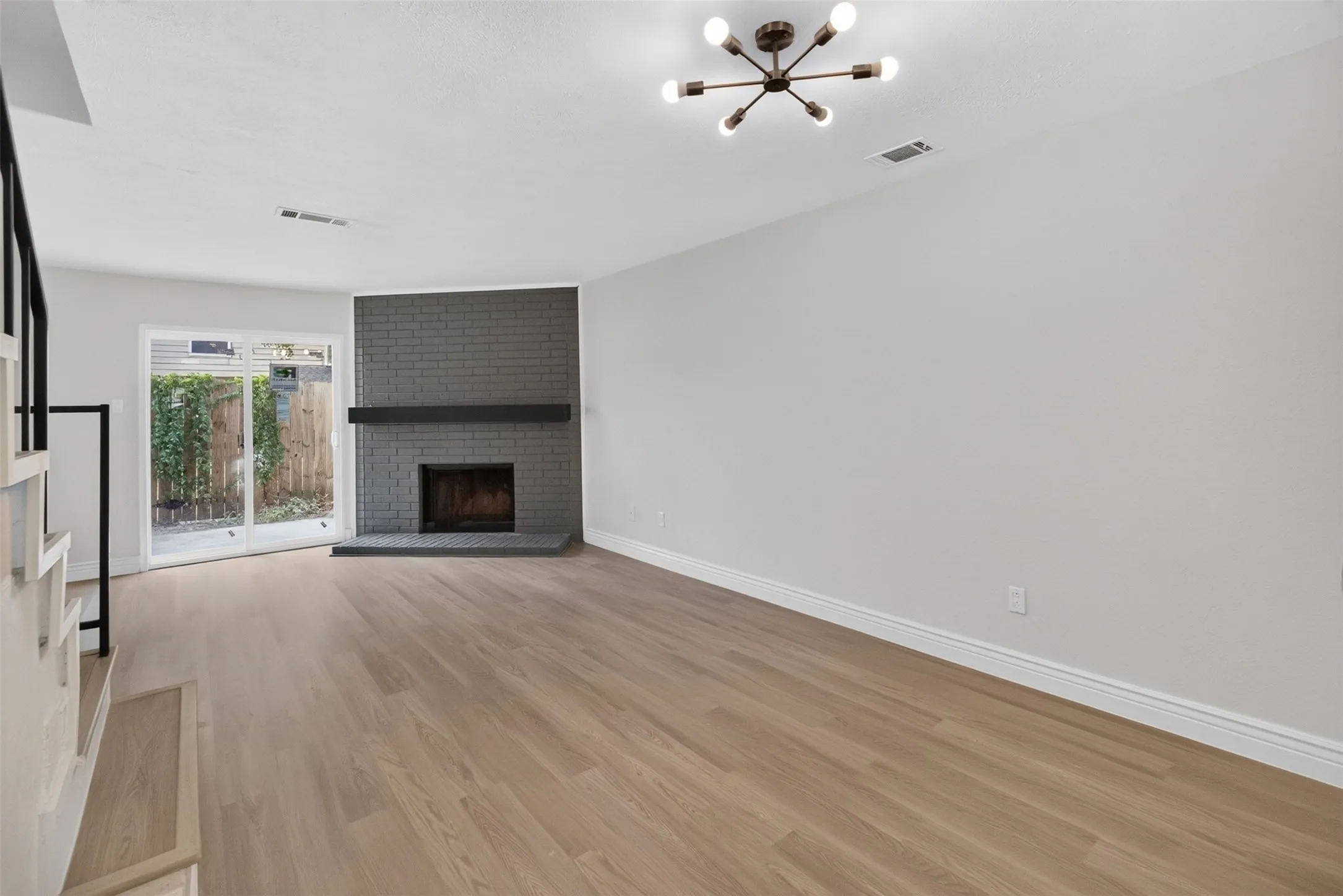 Wood-finish flooring, contemporary ceiling light fixture, sliding glass door, brick fireplace with mantel, and white baseboards
