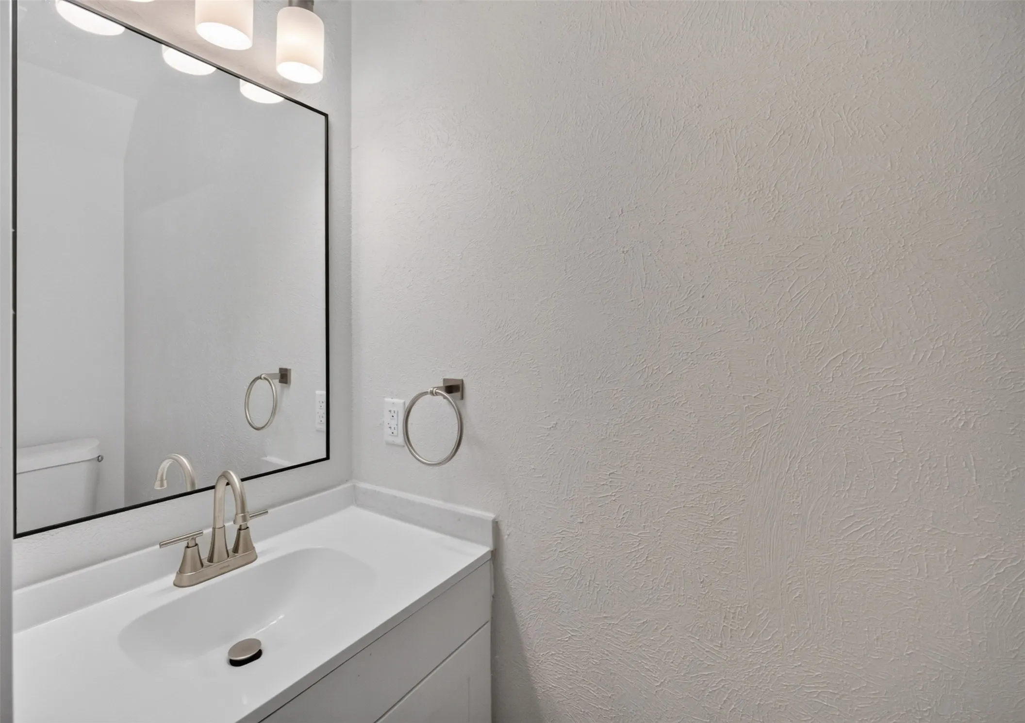 White vanity with an integrated sink, brushed nickel faucet, large framed mirror, and contemporary light fixture