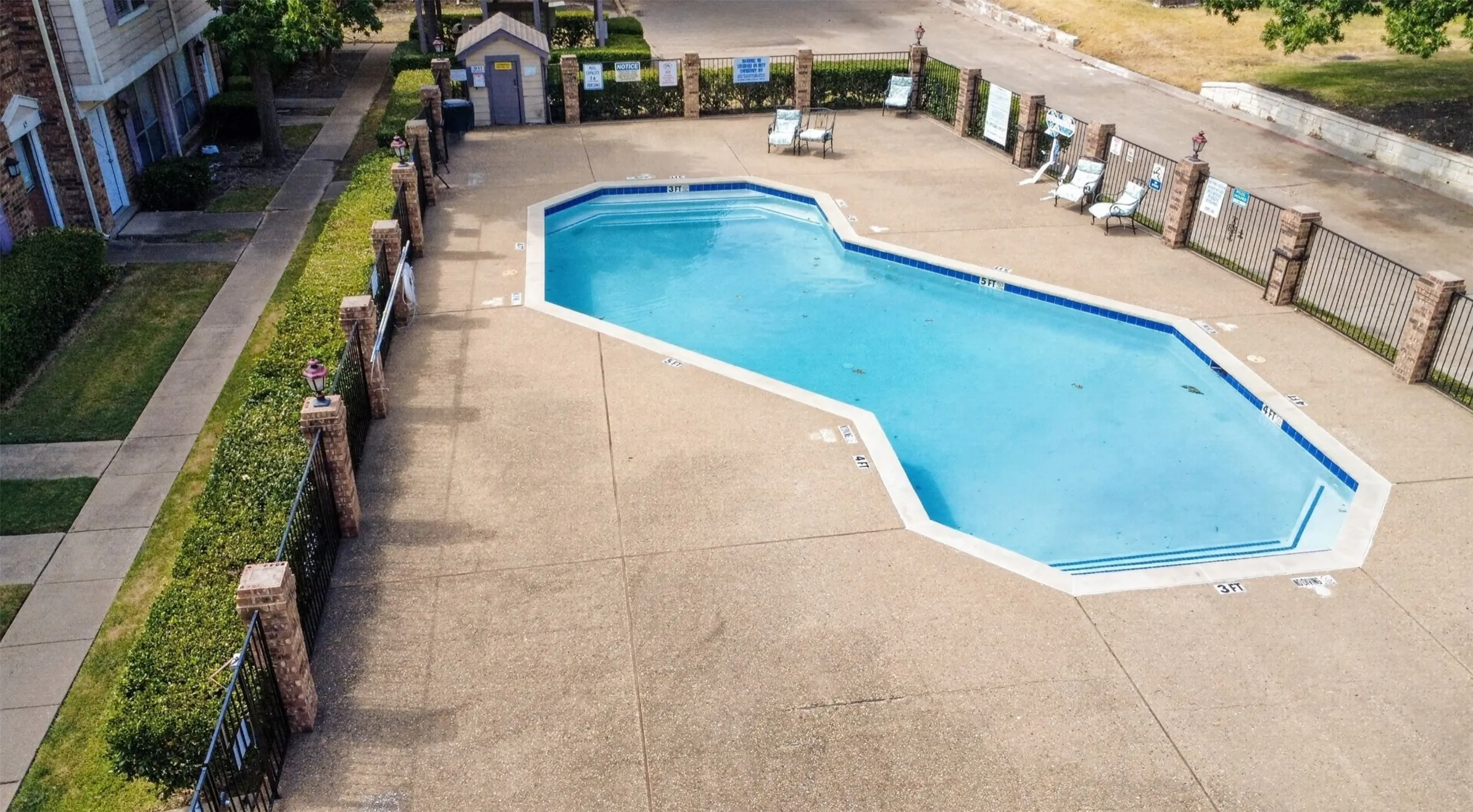 Community swimming pool with concrete decking, perimeter fencing with brick posts, and an adjacent building