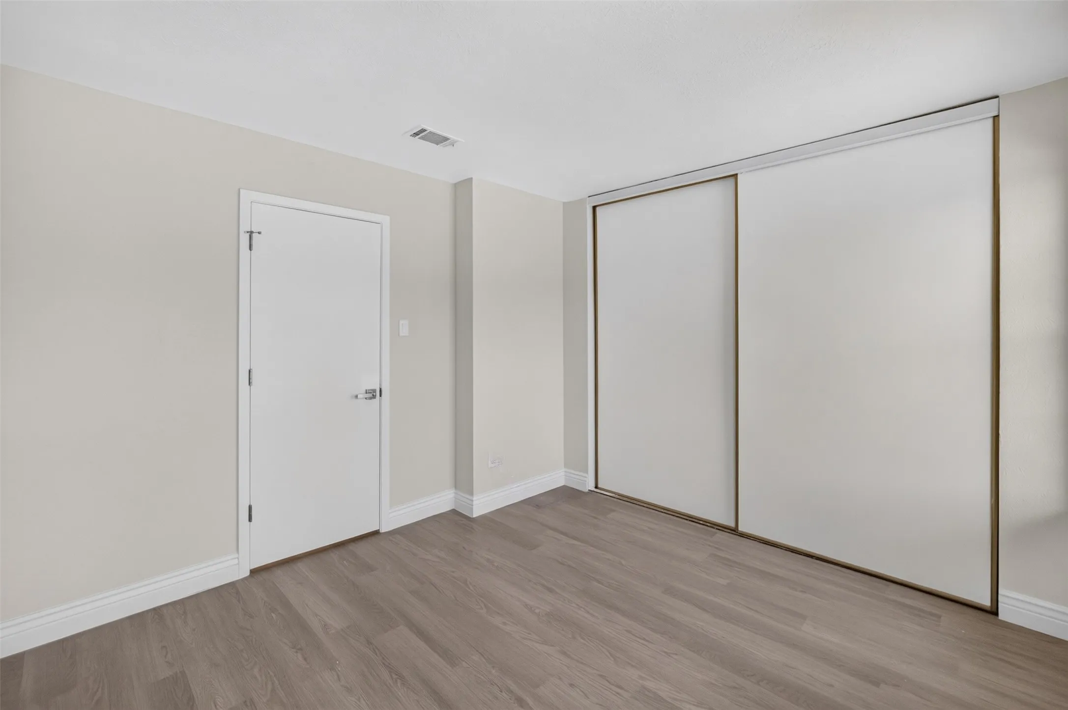 Wood-finish flooring, white baseboards, and built-in sliding closet doors