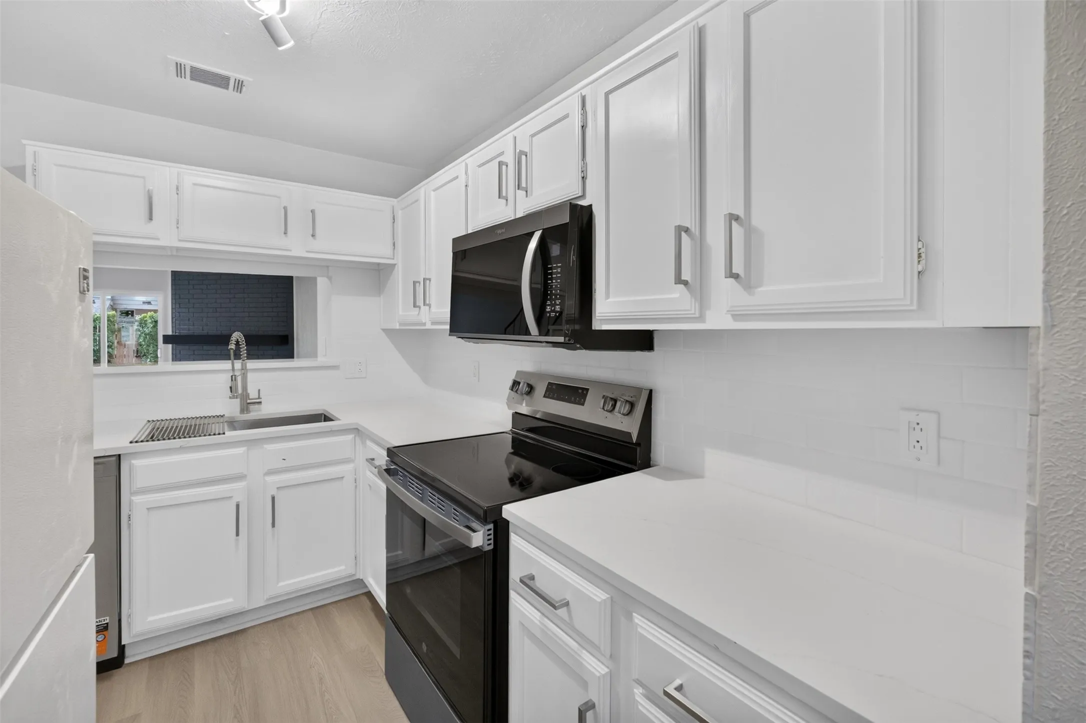 Kitchen featuring white cabinetry, white countertops, stainless steel appliances, a tile backsplash, and wood-finish flooring