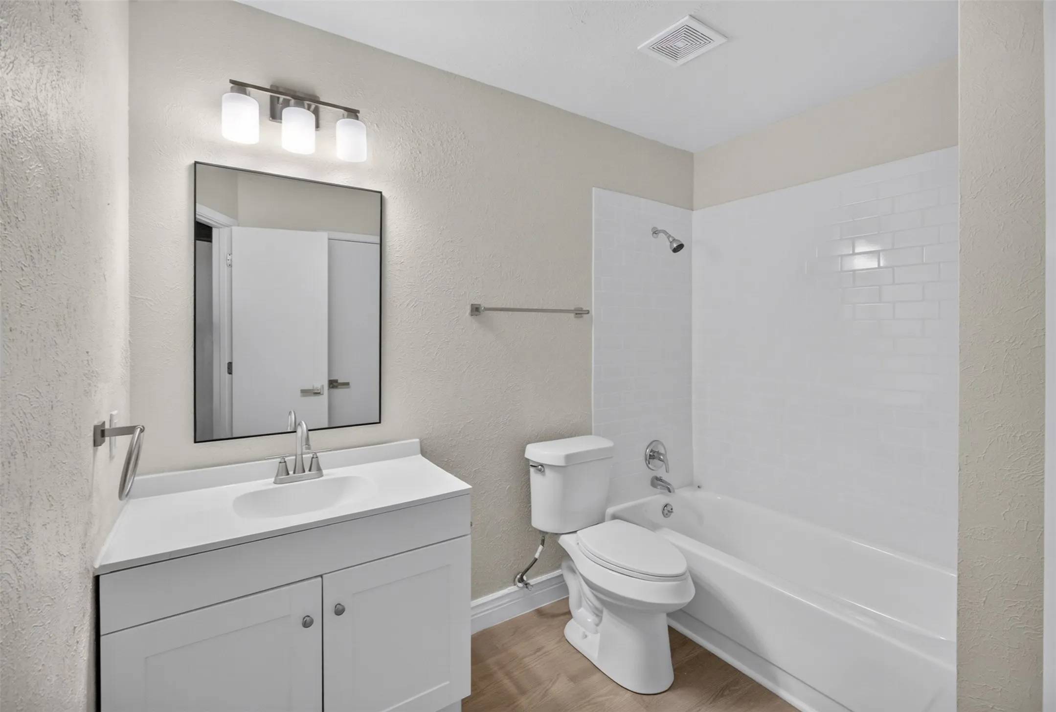 White vanity with a rectangular undermount sink, a framed mirror, and a three-light vanity fixture