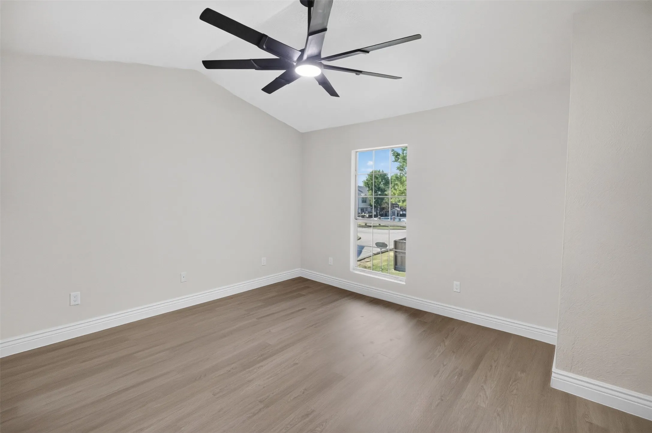 Vaulted ceiling with a contemporary ceiling fan, large window, wood-finish flooring, and white trim
