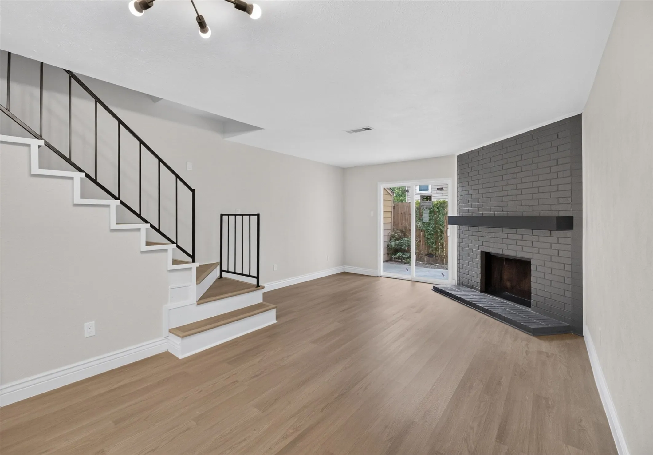 Light wood-finish flooring throughout, a painted brick fireplace with a dark mantel, and a sliding glass door