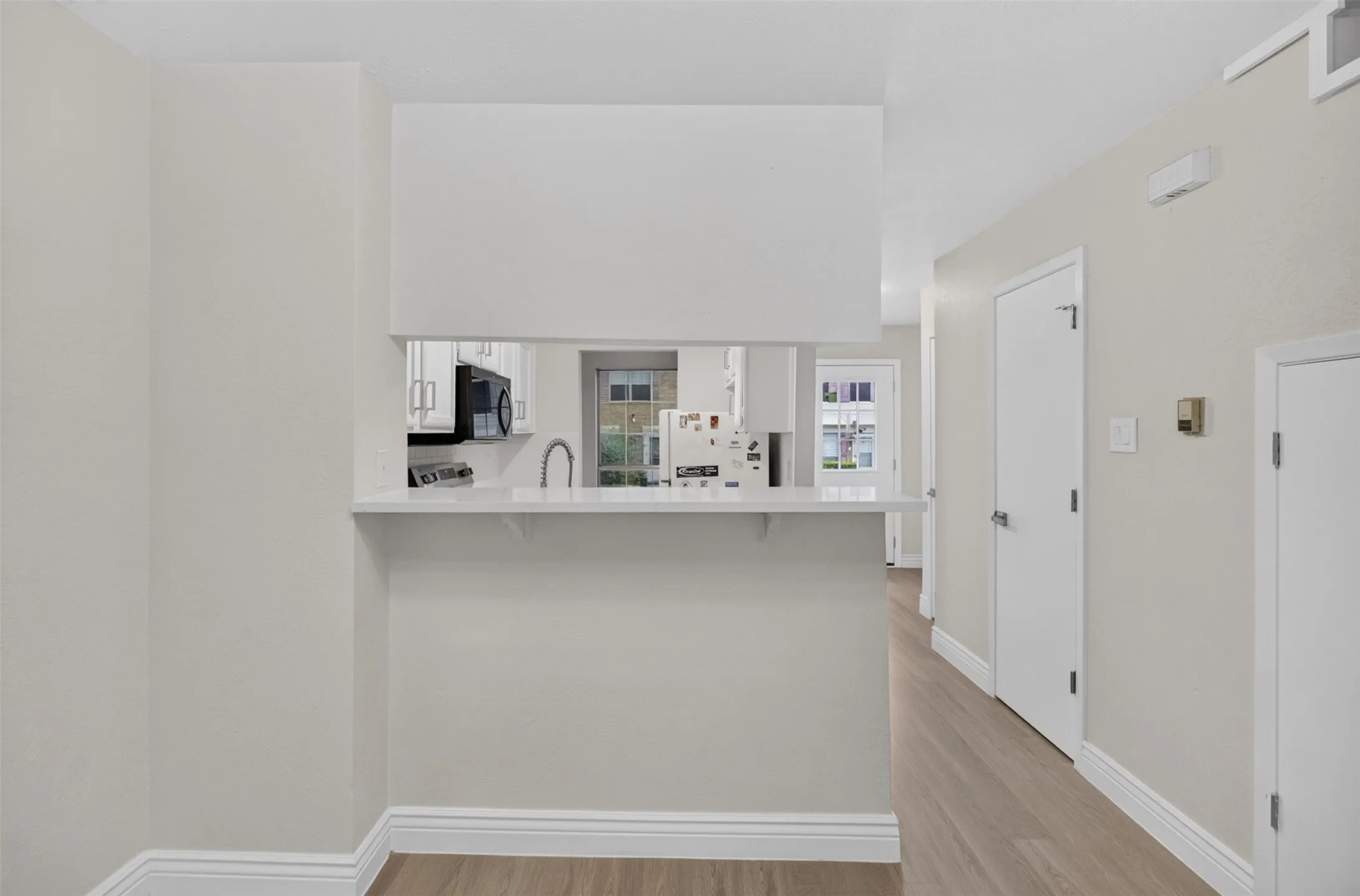 Pass-through counter with light-toned countertop, wood-finish flooring, white doors, and white baseboards
