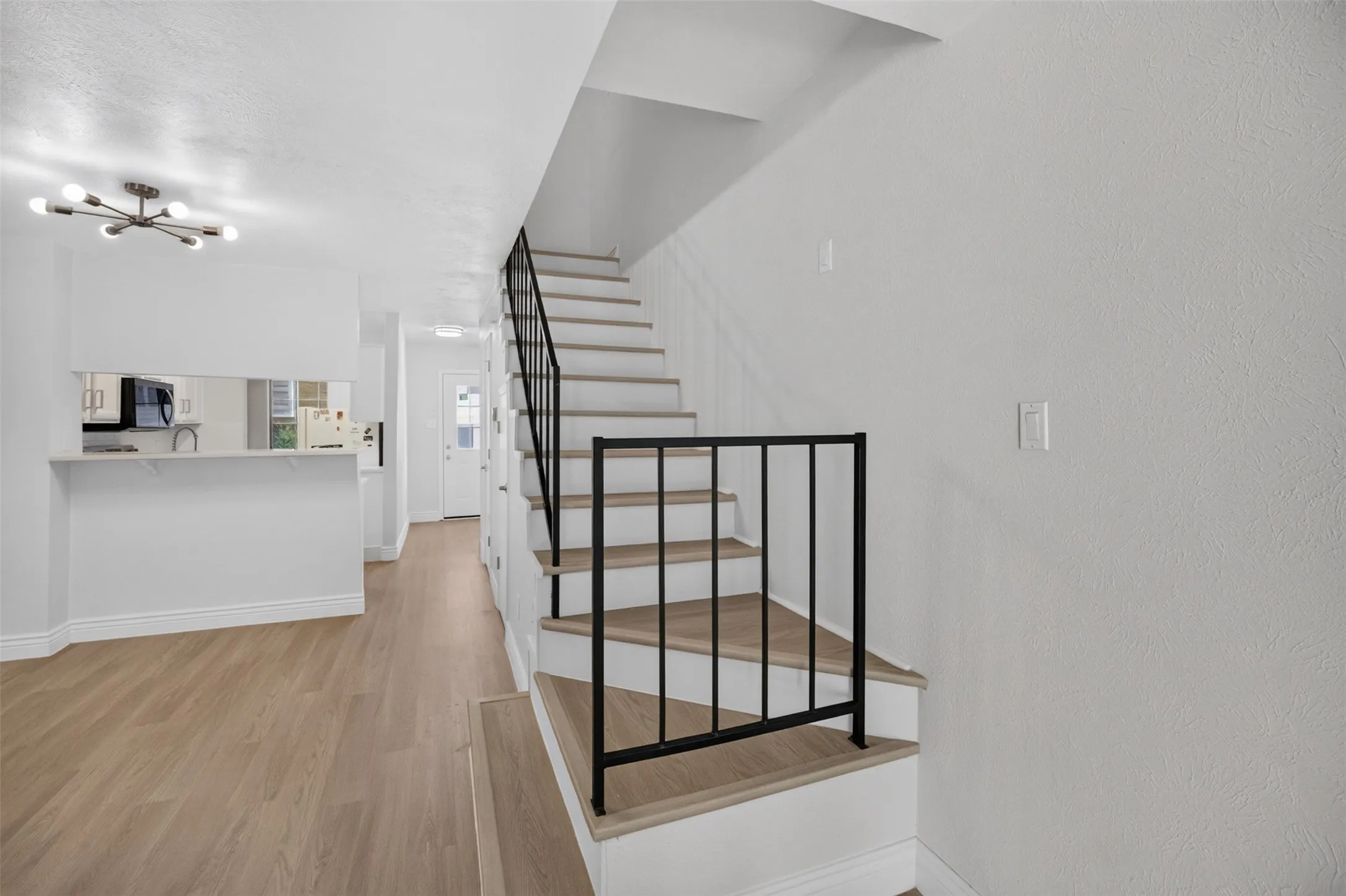 Modern open-concept living area featuring warm wood-finish flooring, white walls, and abundant natural light