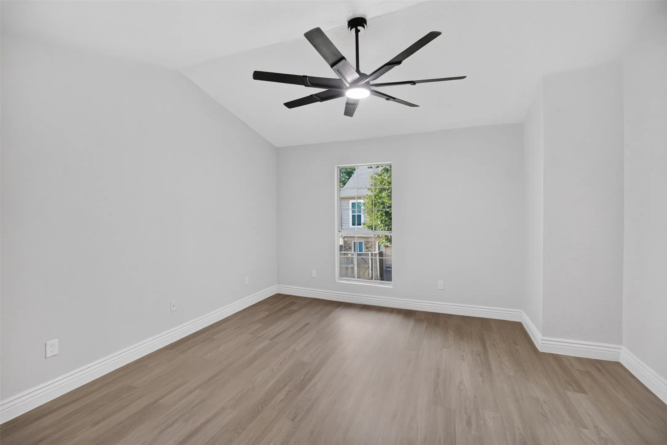 Vaulted ceiling with a contemporary ceiling fan, wood-finish flooring, and white baseboards