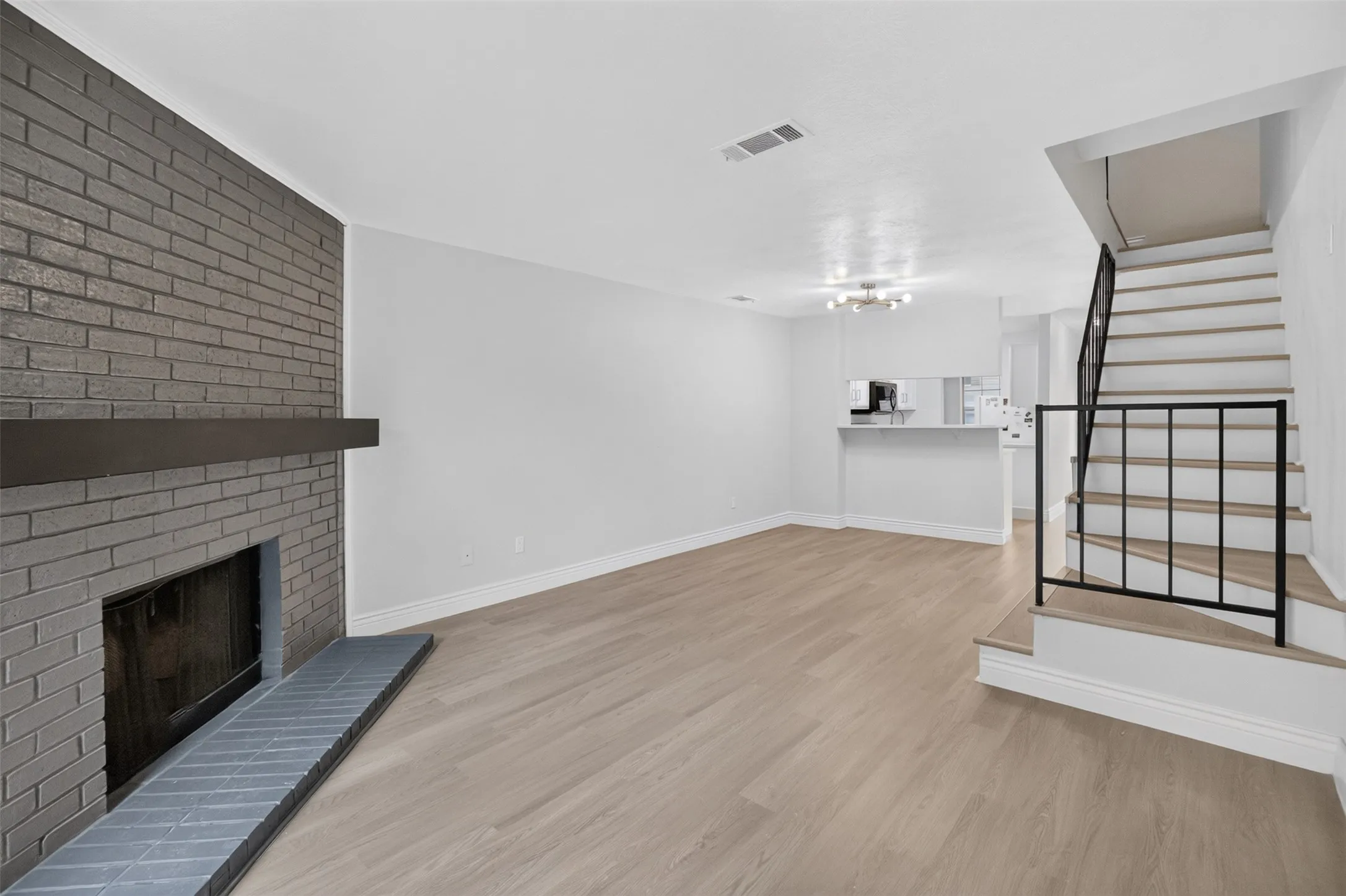 Painted brick fireplace with mantel, wood-finish flooring, staircase with metal railing, and a breakfast bar