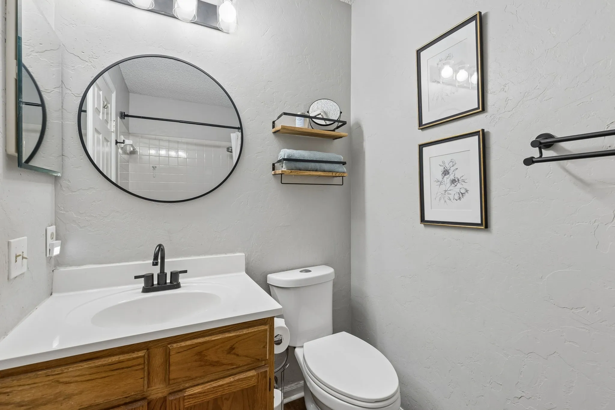 Full Bath with Modern Black Fixtures, Round Mirror and Decorative Shelving