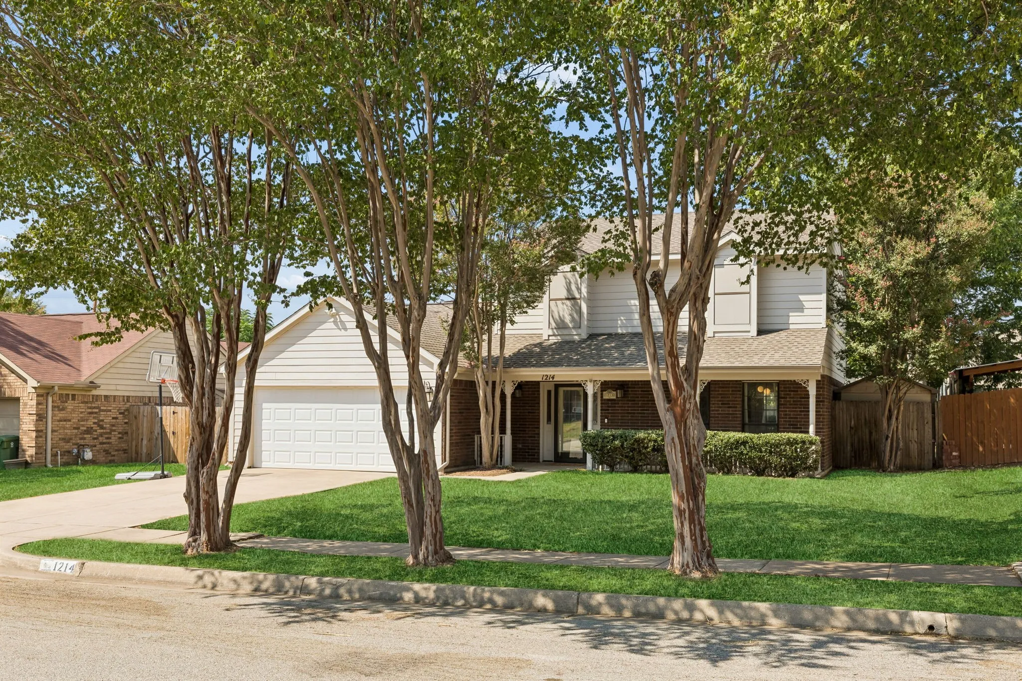 Welcoming Two-Story Exterior with Mature Shade Trees and Brick Accents on Front Porch