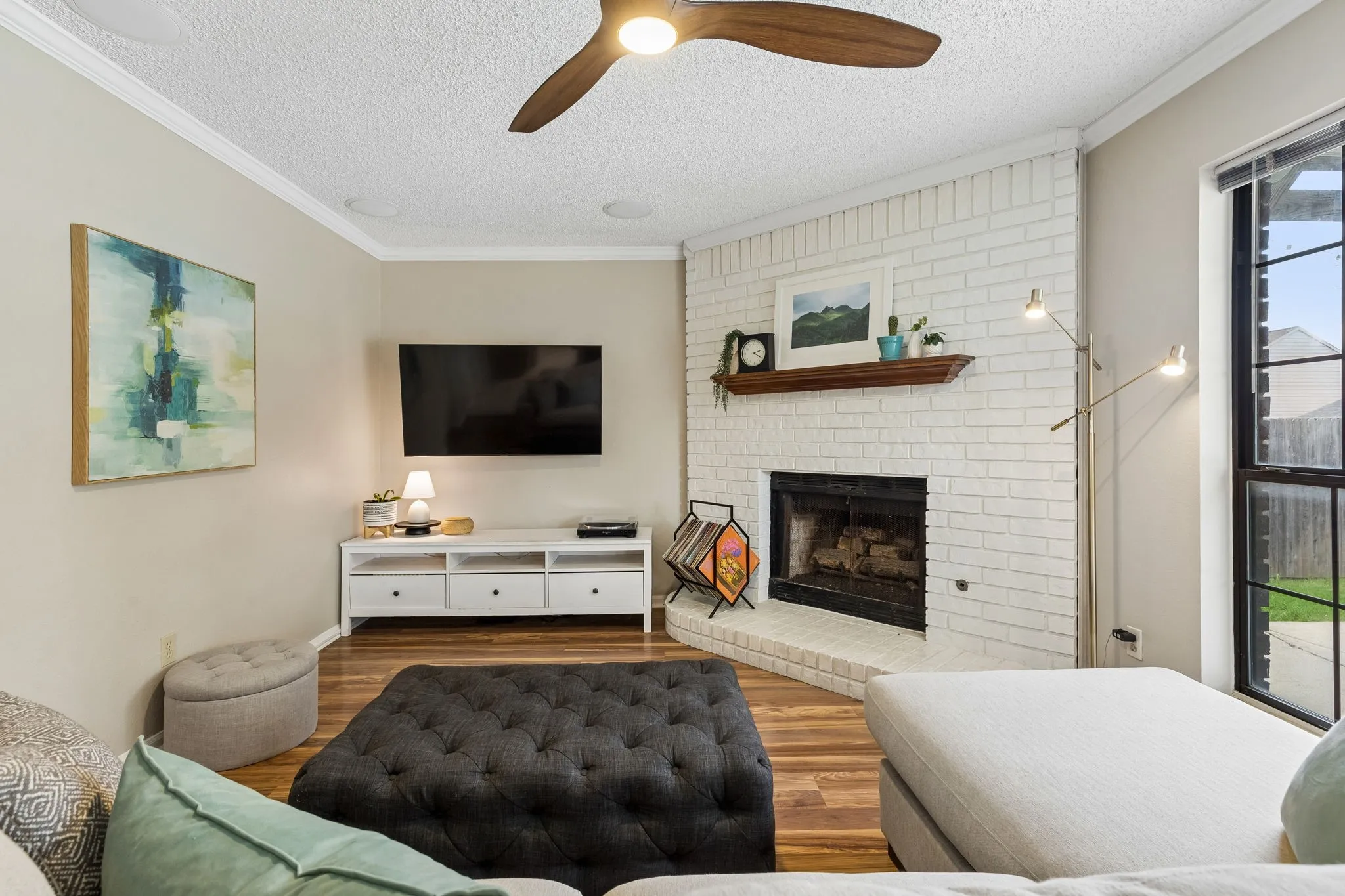 Cozy Living Room Featuring a Painted Brick Fireplace, Wood-Look Flooring and Wall-Mounted TV