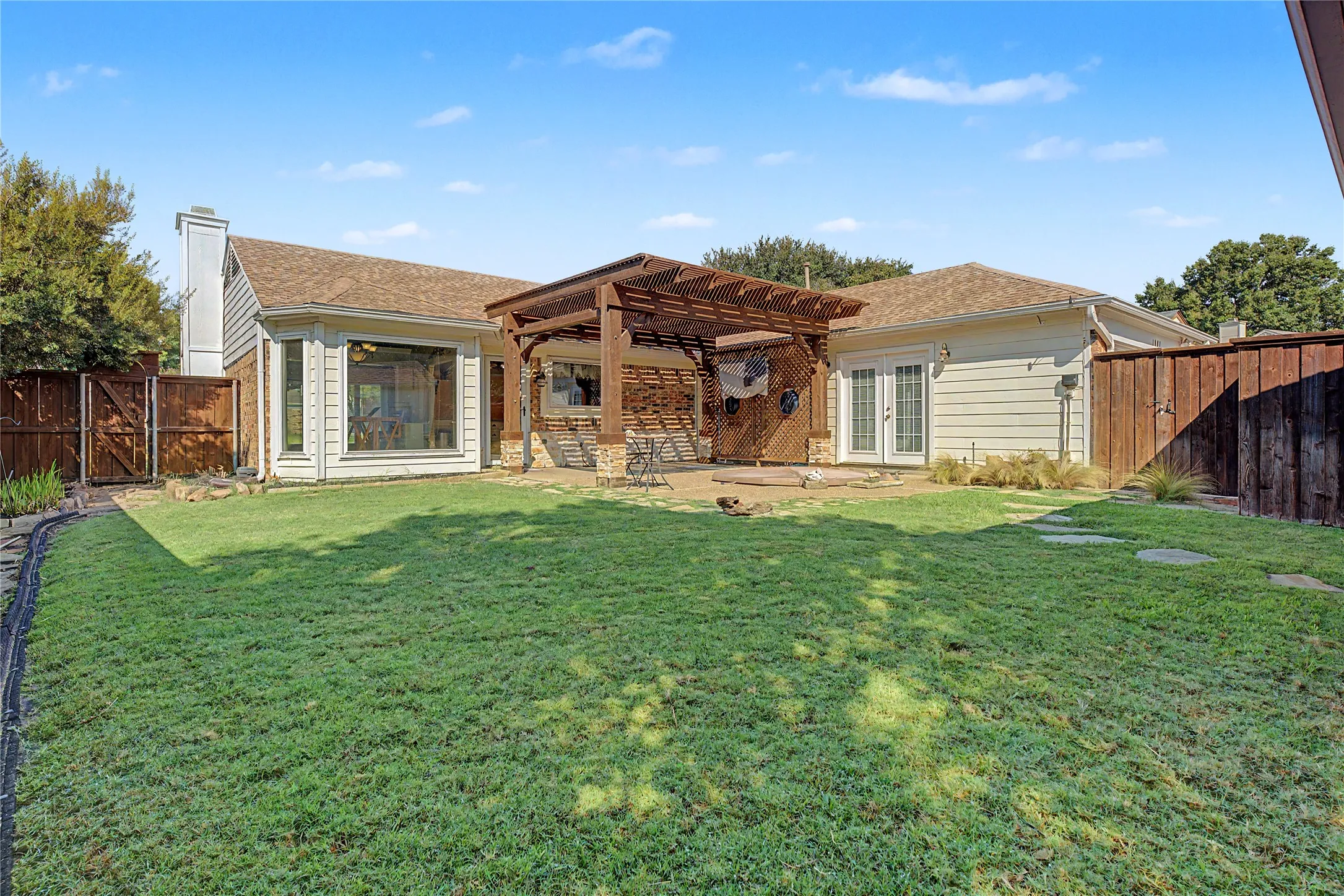 Expansive lawn with stepping stones, wood pergola with stone-clad pillars, full-height windows, and double French doors
