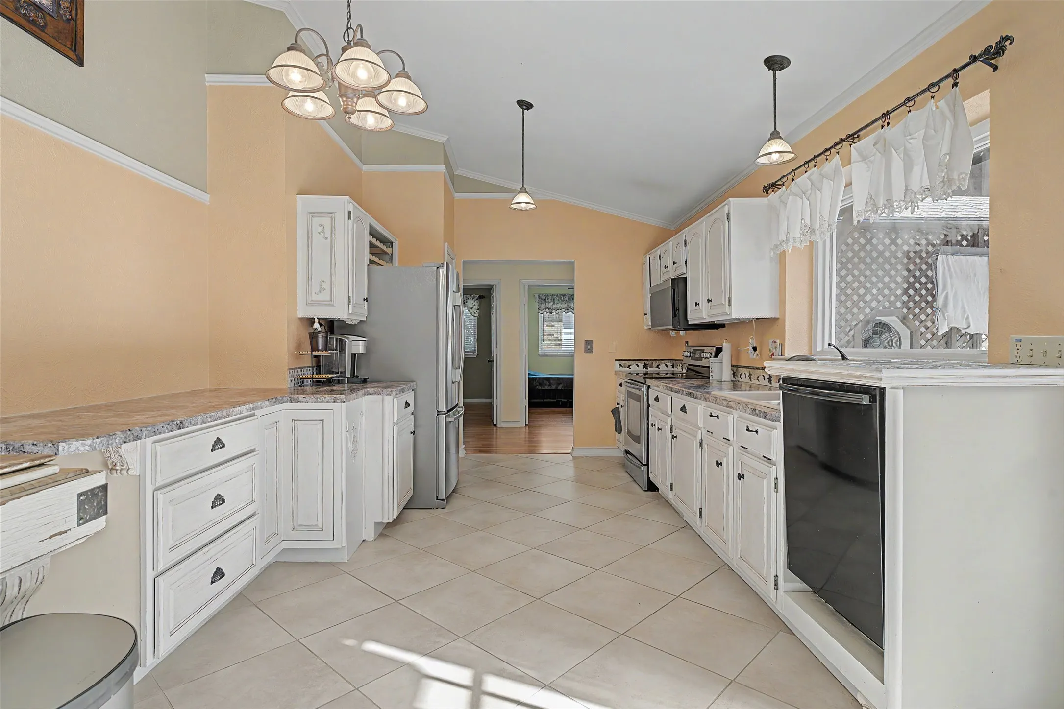 Galley kitchen featuring white cabinetry, light-toned countertops, stainless steel refrigerator, and a built-in dishwasher